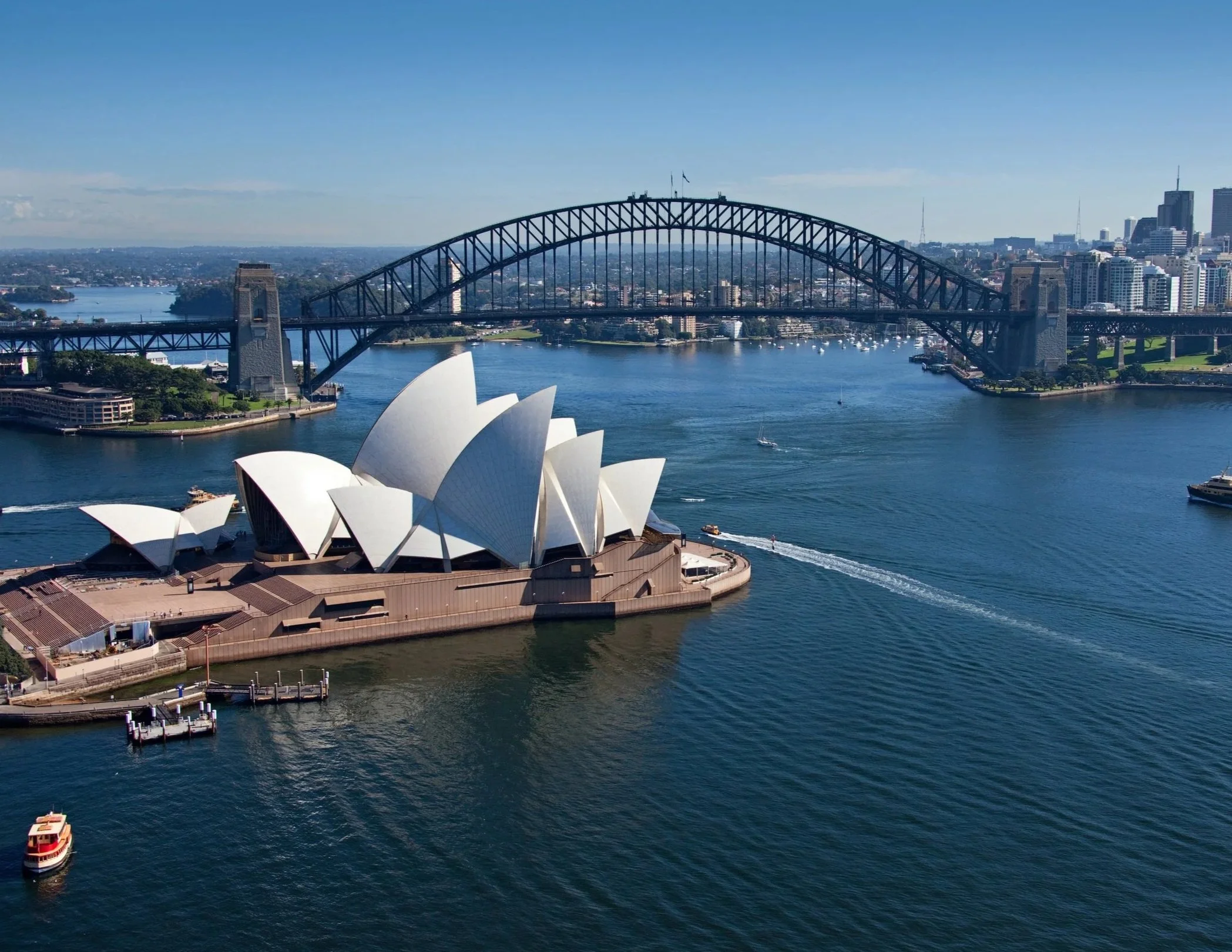 Aerial view of Sydney Opera House with Sydney Harbour Bridge and city skyline in the background on a clear day.