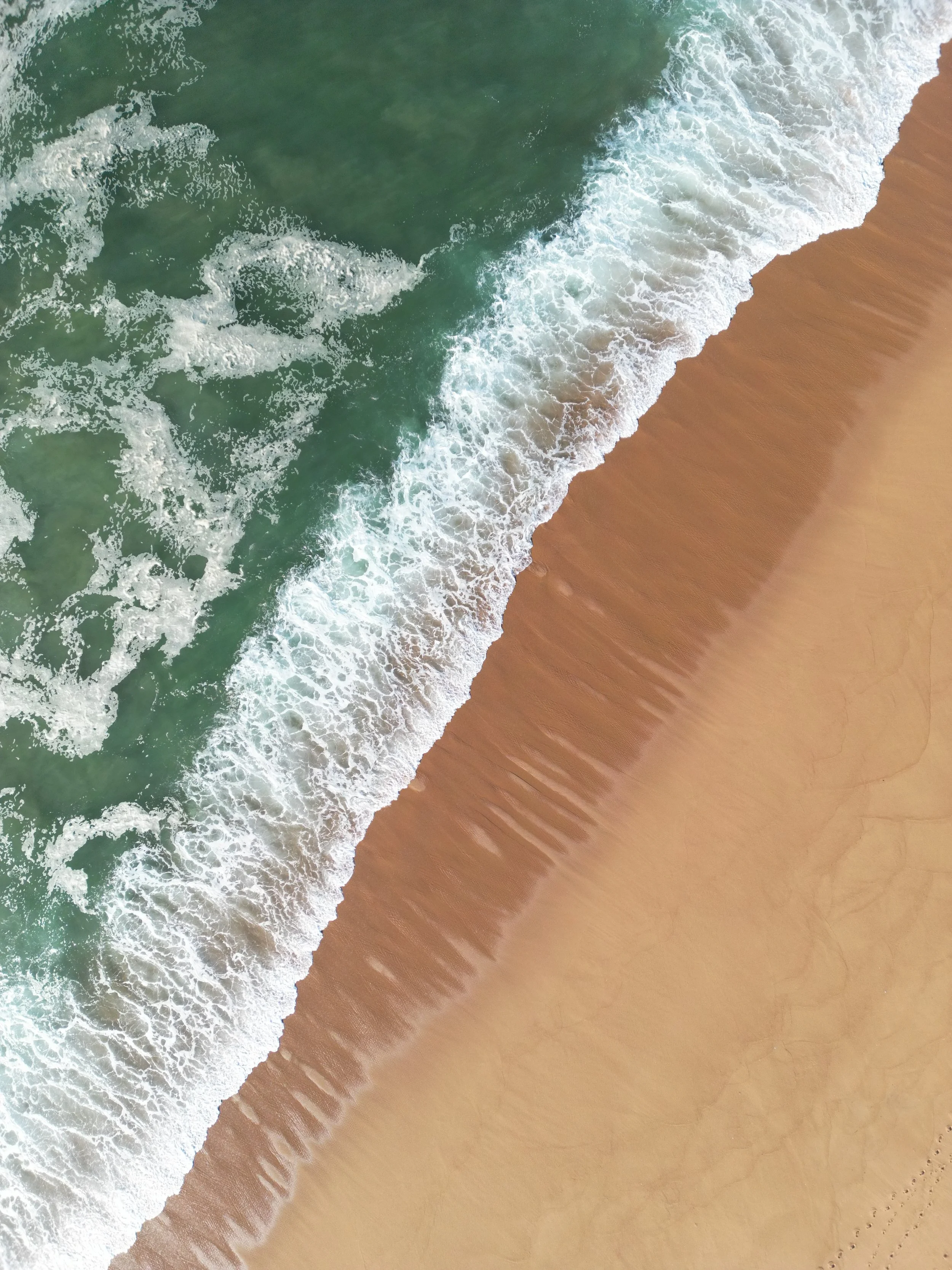 An aerial view of a sandy beach with ocean waves crashing onto the shore.