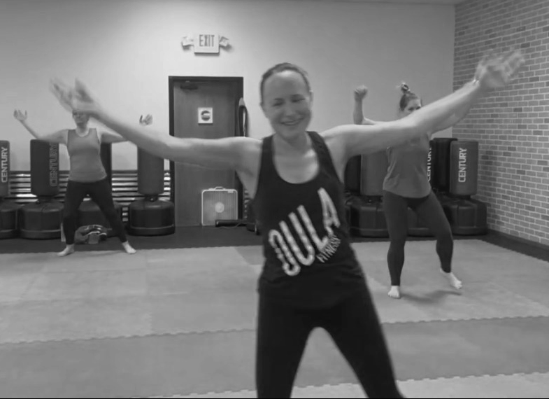 Women participating in a fitness class, stretching with arms out wide, in a gym or fitness studio.