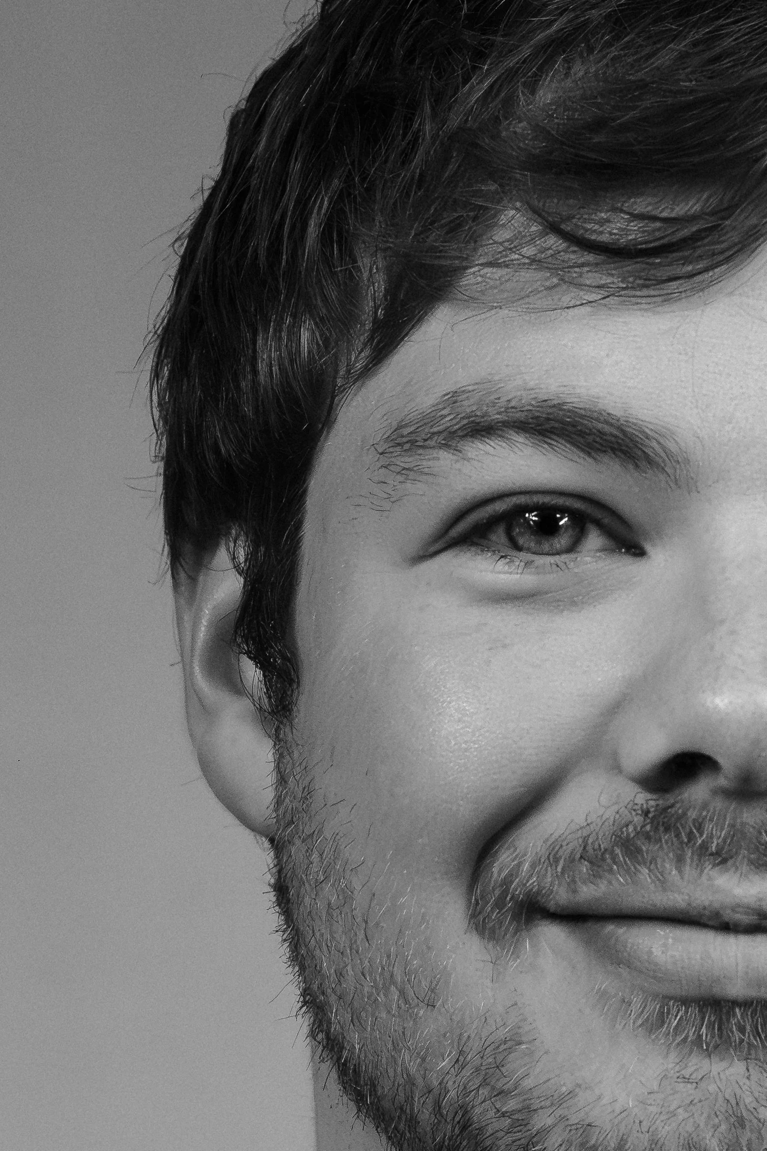 Close-up van een jongeman met donker haar, lichte huid, een beetje gezichtshaar en een glimlach die gedeeltelijk zichtbaar is.