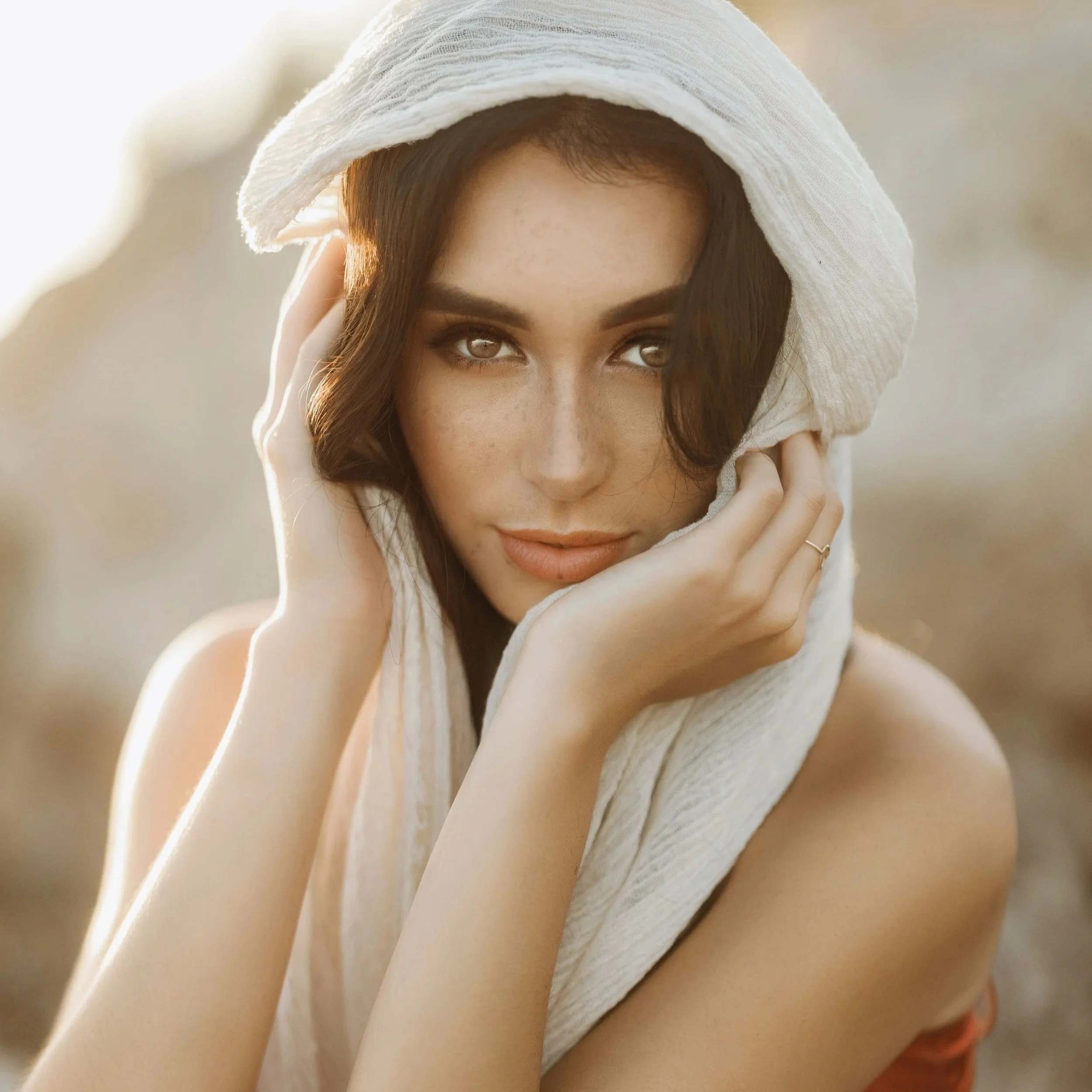Close-up of a young woman with dark hair, wearing a white towel on her head, looking into the camera with a slight smile.