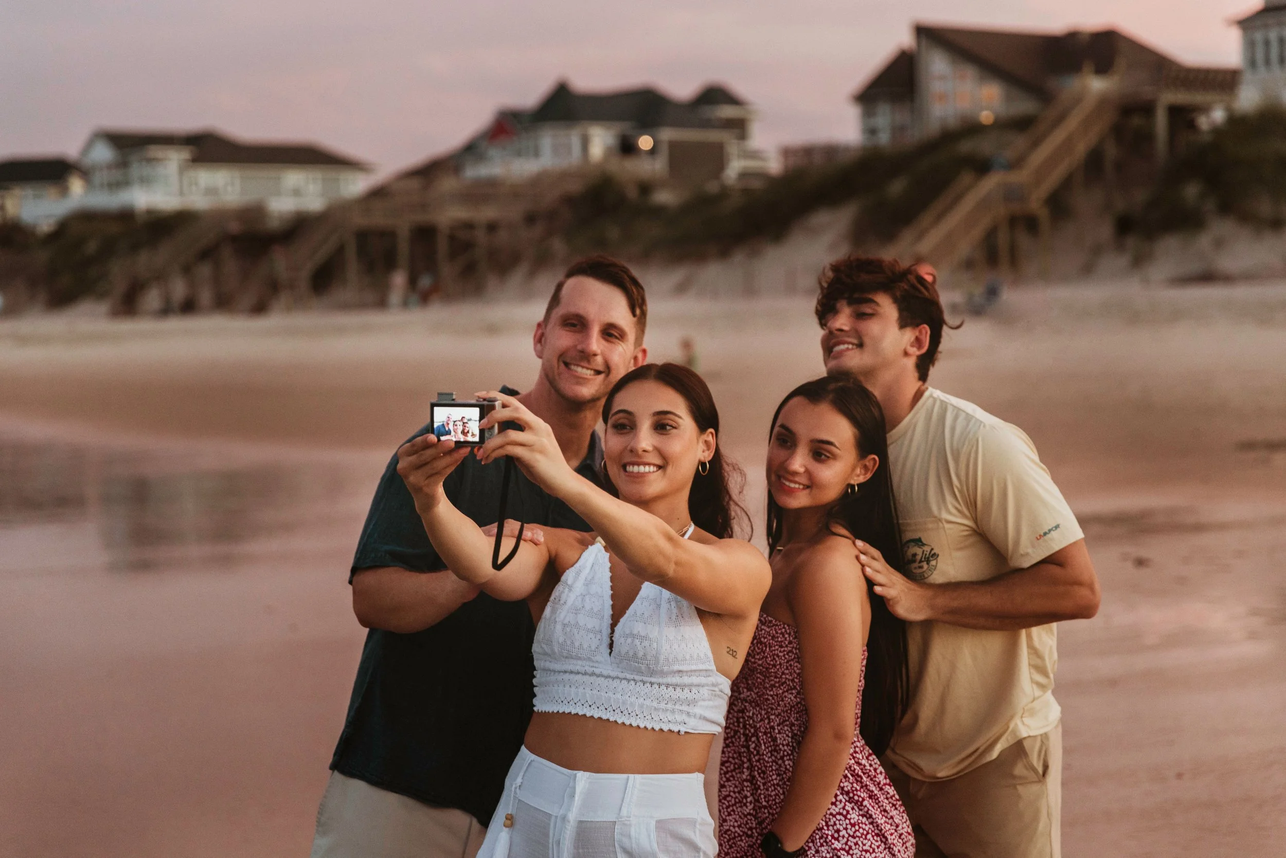 Group of four young adults taking a selfie on the beach at sunset