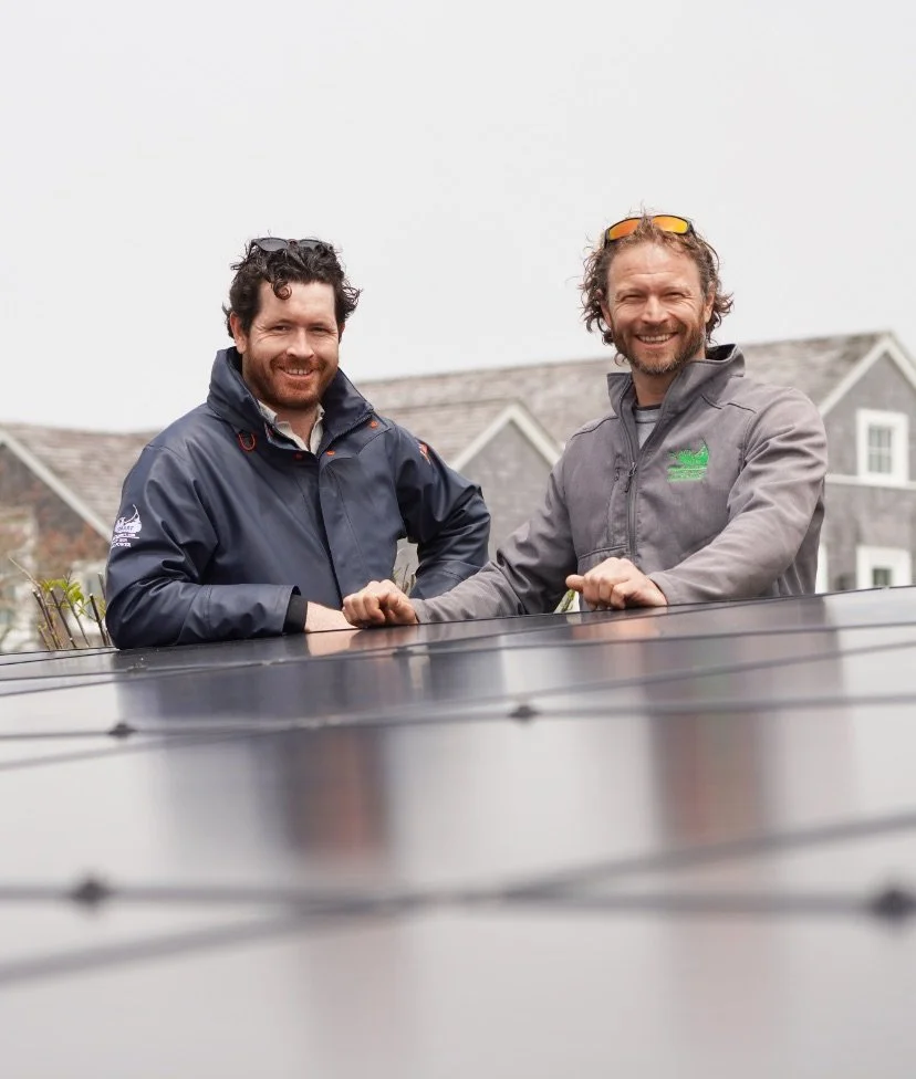 ACK Smart's Tobias Glidden and Zach Dusseau behind solar panels smiling