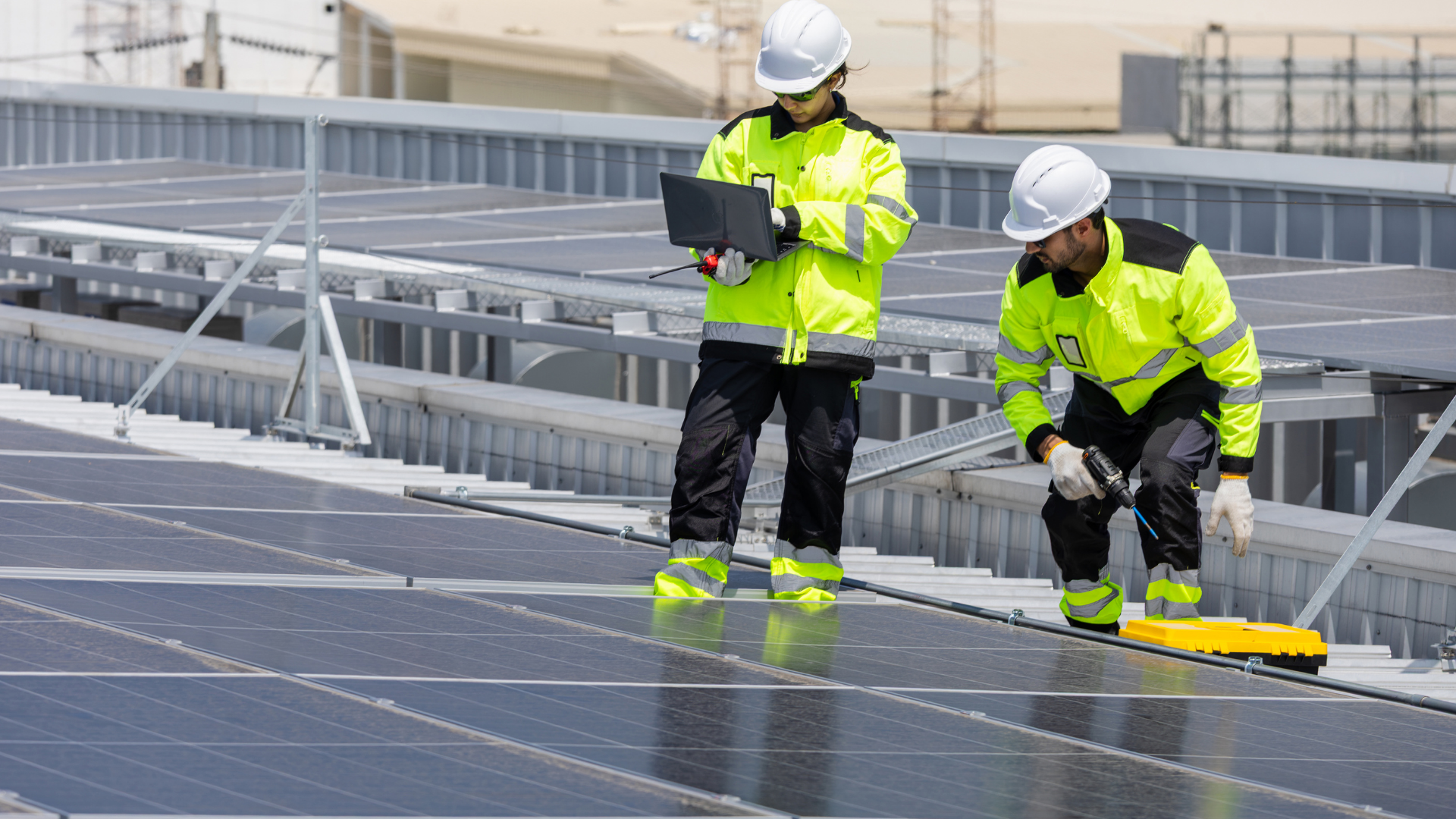 Dos trabajadores con casco y ropa de seguridad instalando paneles solares en un techo de construcción.