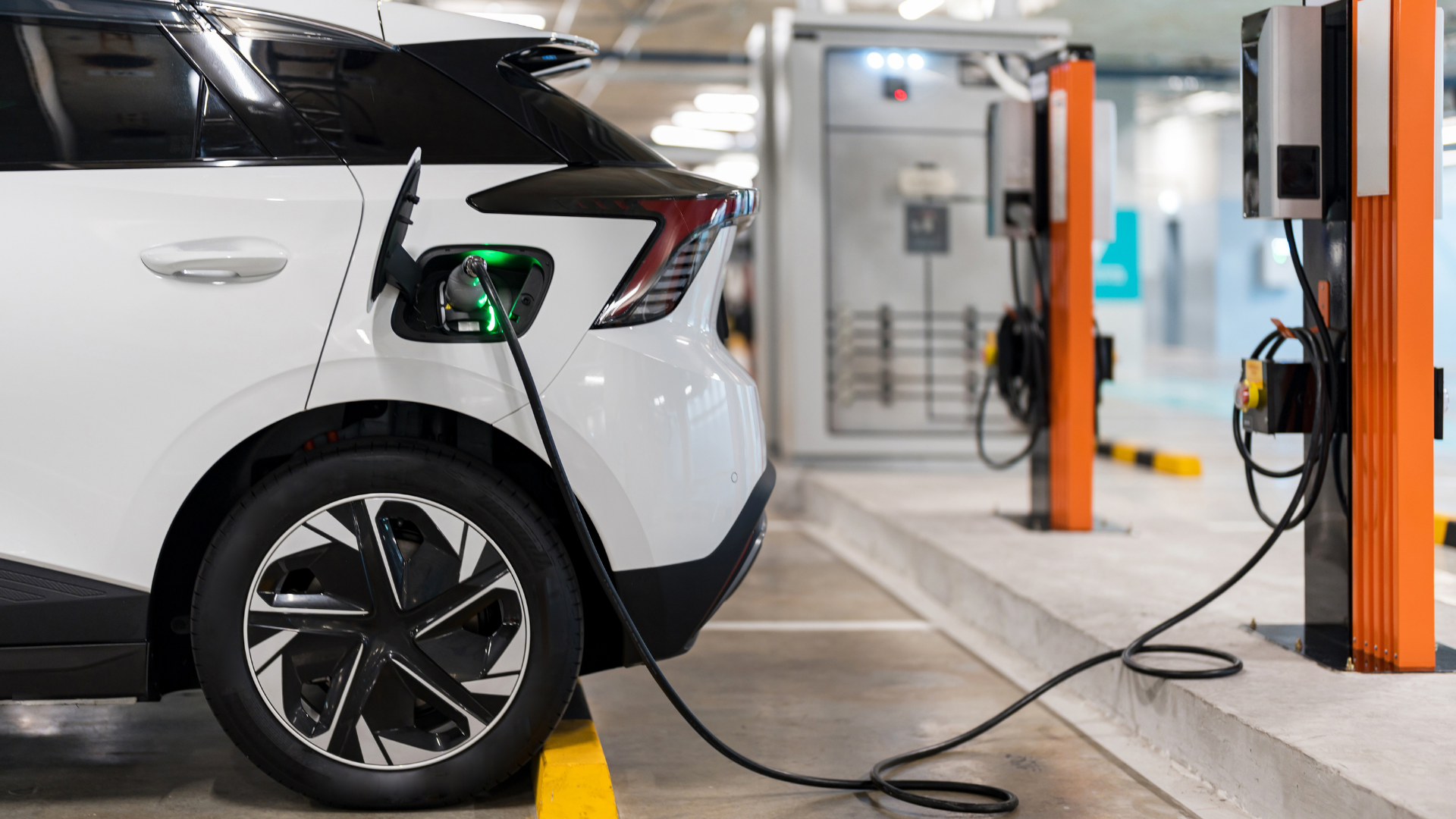 carro eléctrico en estación de carga, conectado y siendo cargado en un espacio de estacionamiento con equipo de carga eléctrico en un garaje o centro de recarga.