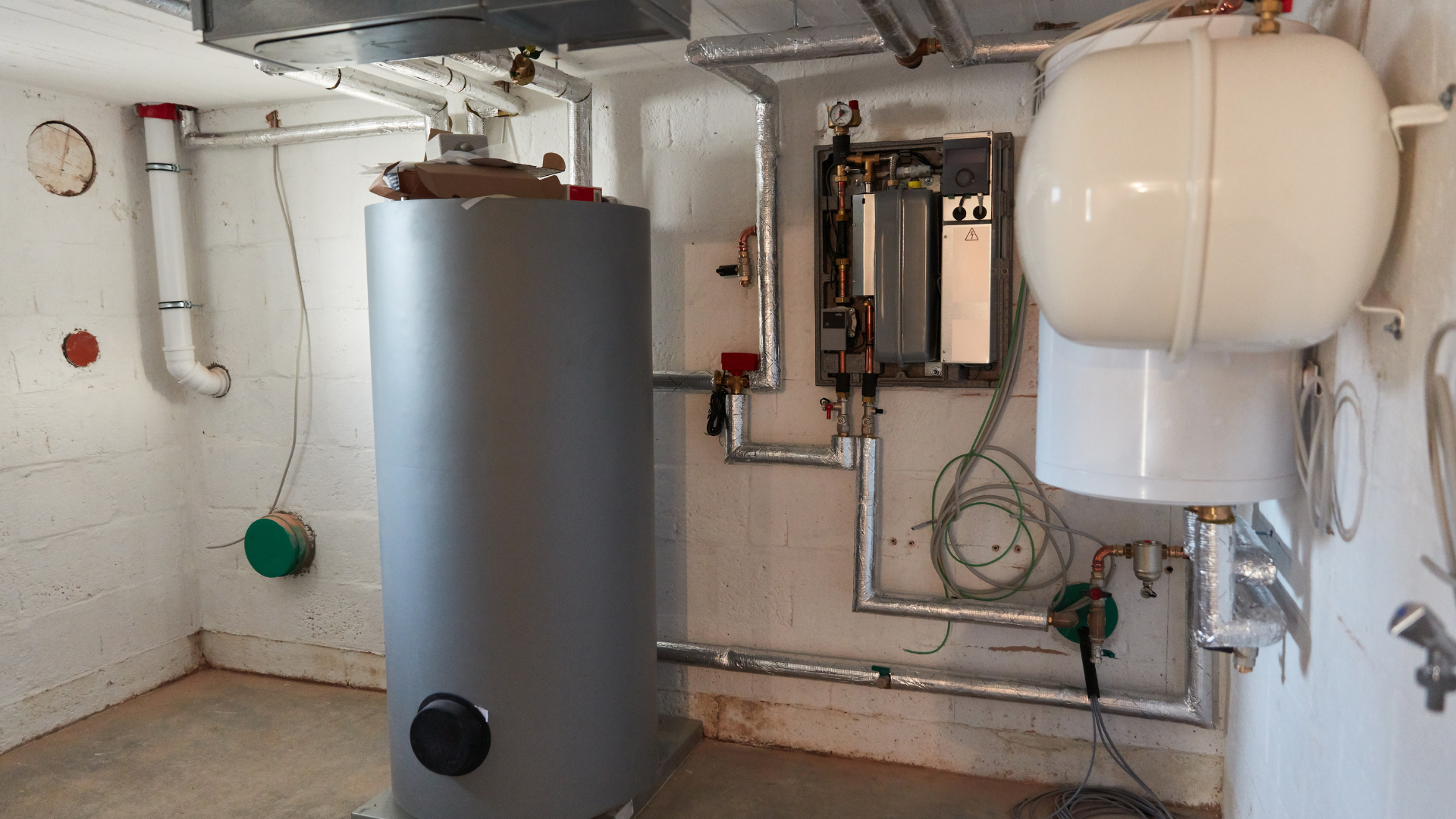 Sistema de calefacción y agua caliente, con tanque y componentes de plomería en una habitación de construcción.
