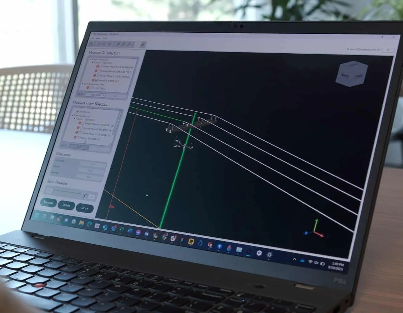 A laptop displaying 3D modeling software with wireframe models of electrical power lines and towers.