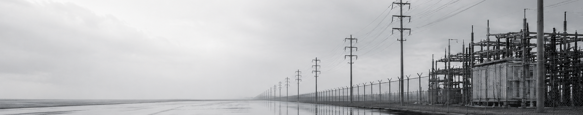 Landscape view of a solar farm with electrical power lines and a chain-link fence under a cloudy sky.