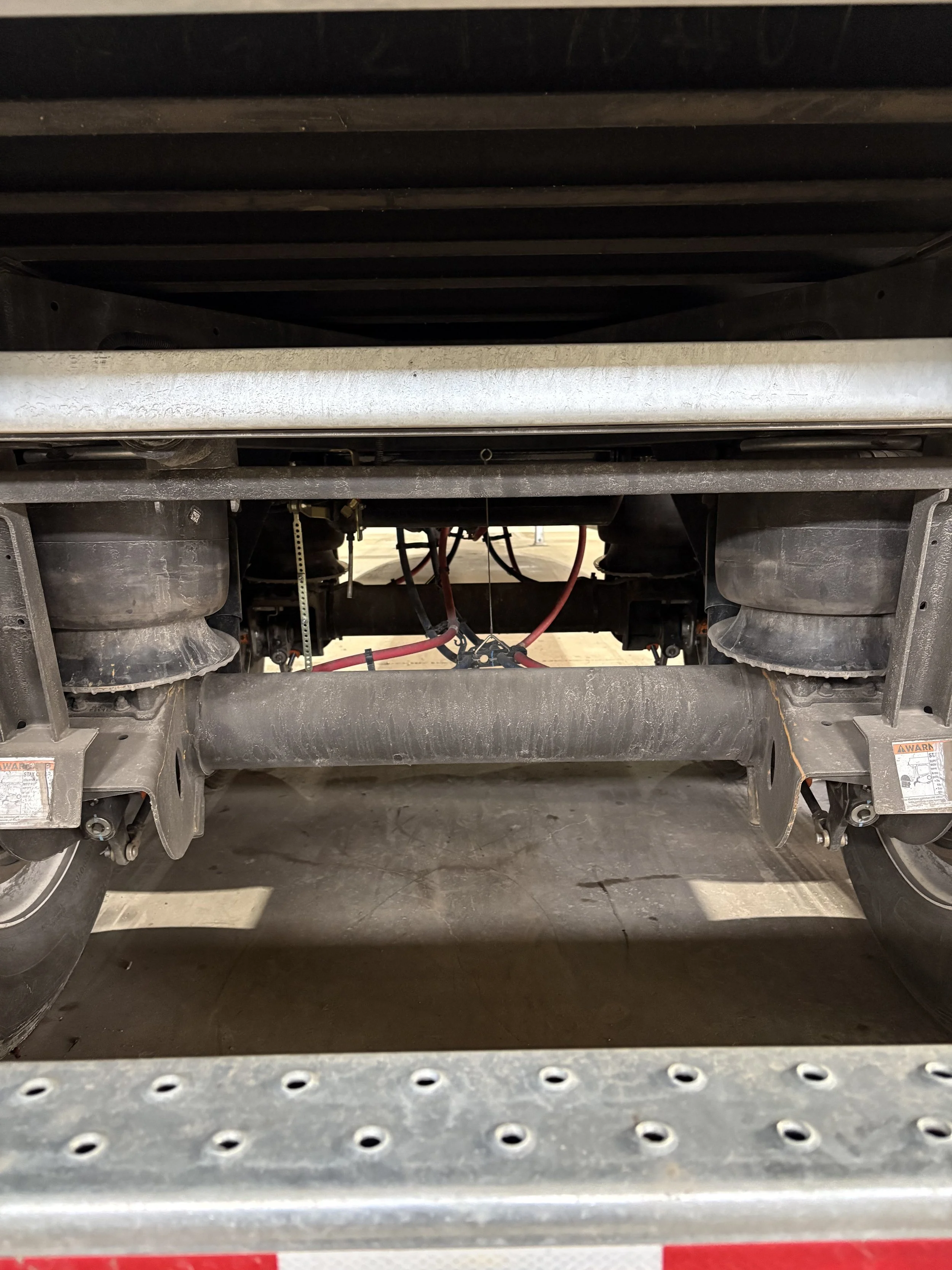 The underside of a flatbed truck showing the wheels, suspension, and some wiring and mechanical components.