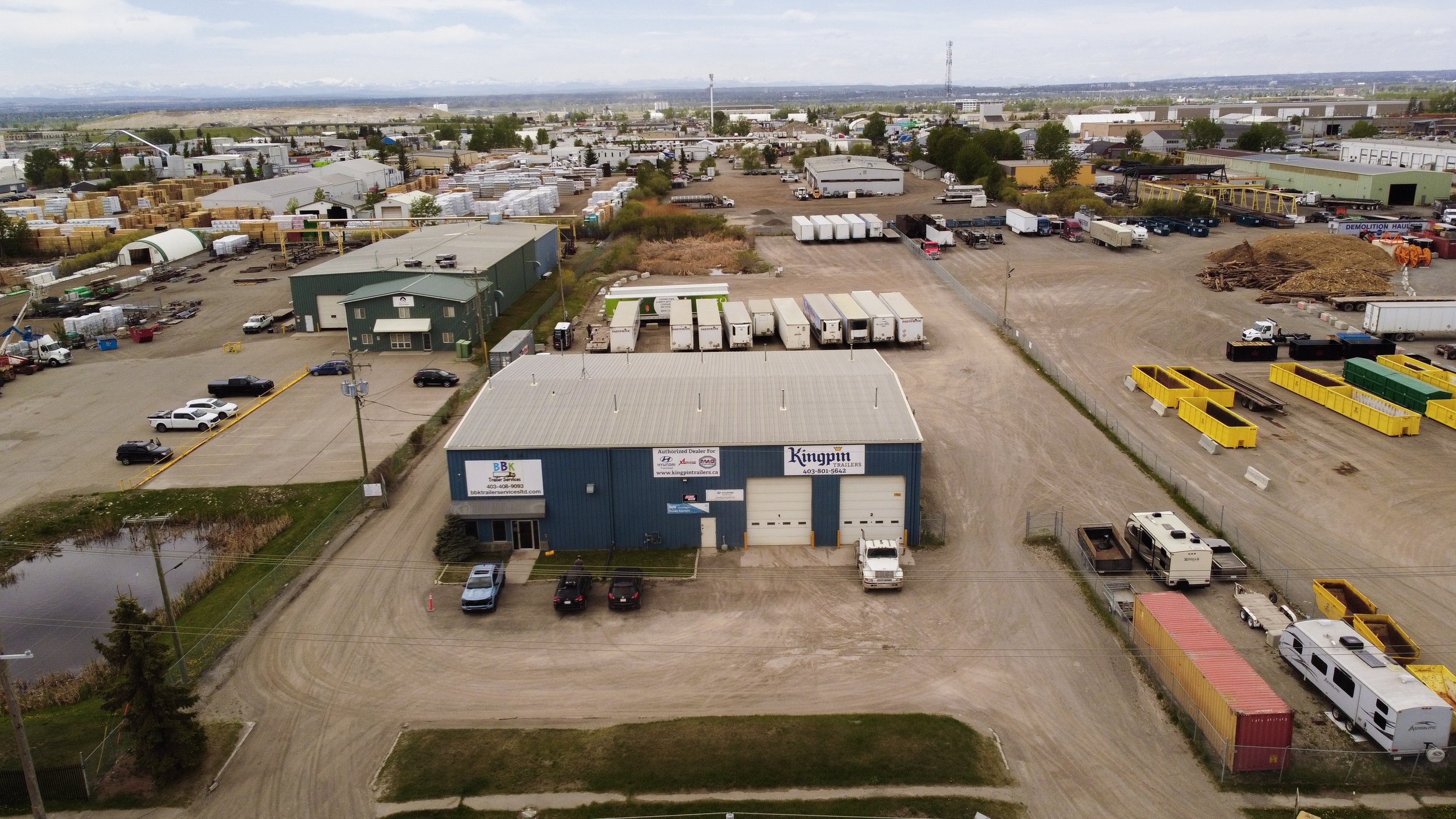 Aerial view of a logistics and storage yard with various trailers, trucks, storage bins, and industrial buildings under a cloudy sky.