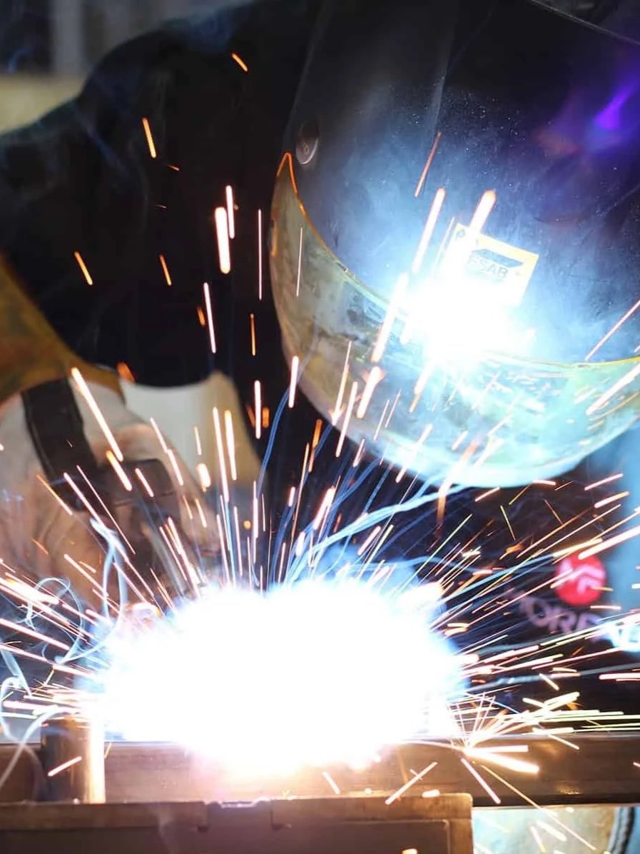A person welding metal, producing sparks and a bright light.