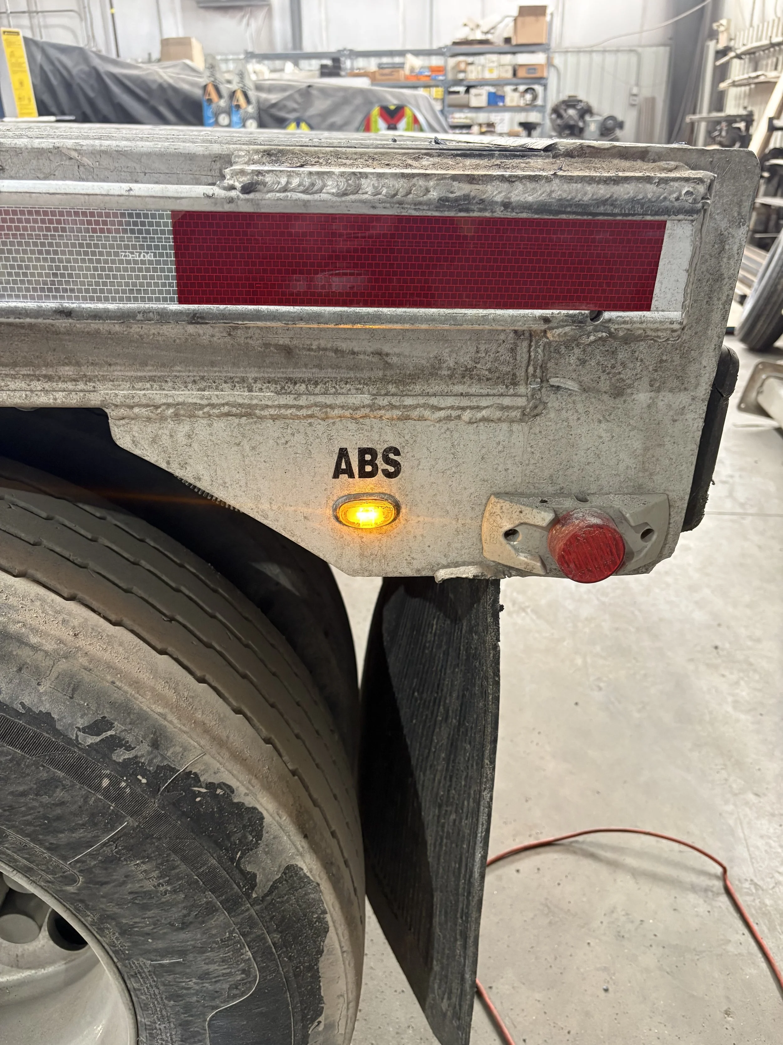 Close-up of a vehicle's rear tire and metal compartment with ABS label and orange indicator light, in a workshop setting.