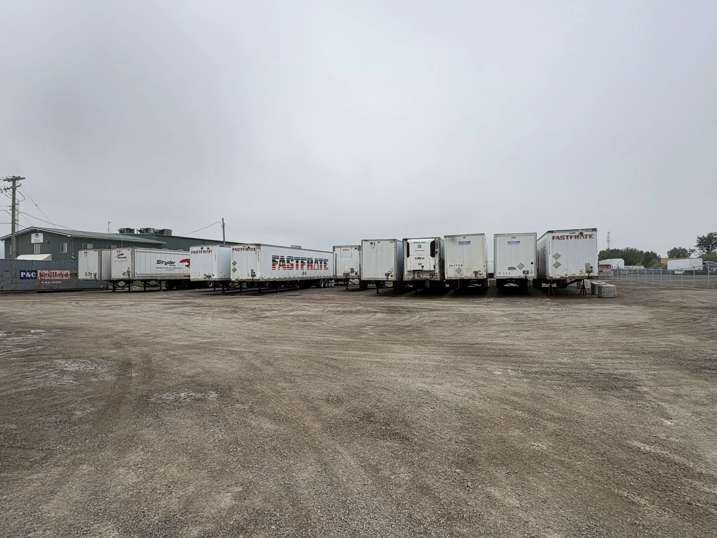 Row of semi-truck trailers parked in a lot on a cloudy day, with a muted sky overhead.