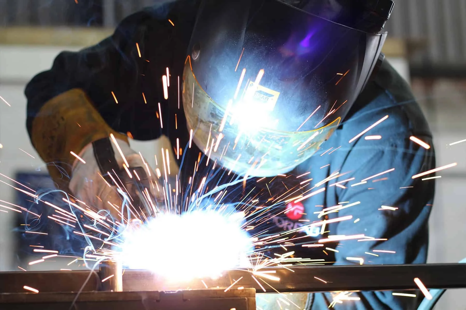 A person welding metal, wearing protective gear including a welding helmet and gloves, sparks flying during the welding process.