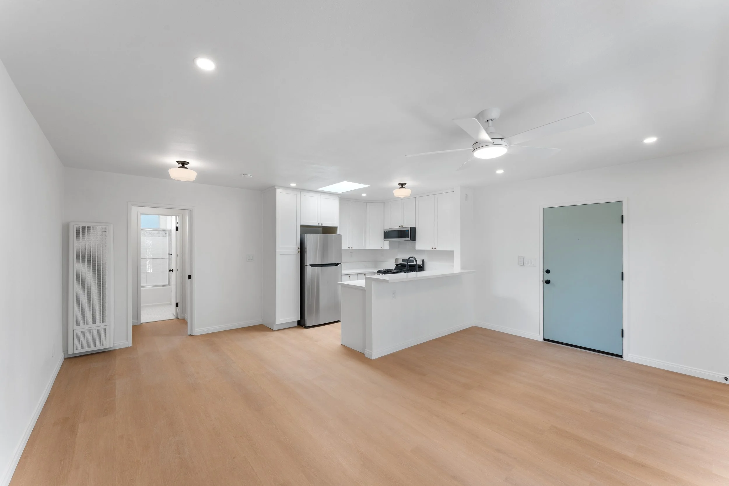 Empty modern kitchen with white cabinets, stainless steel appliances, a ceiling fan, and hardwood flooring.