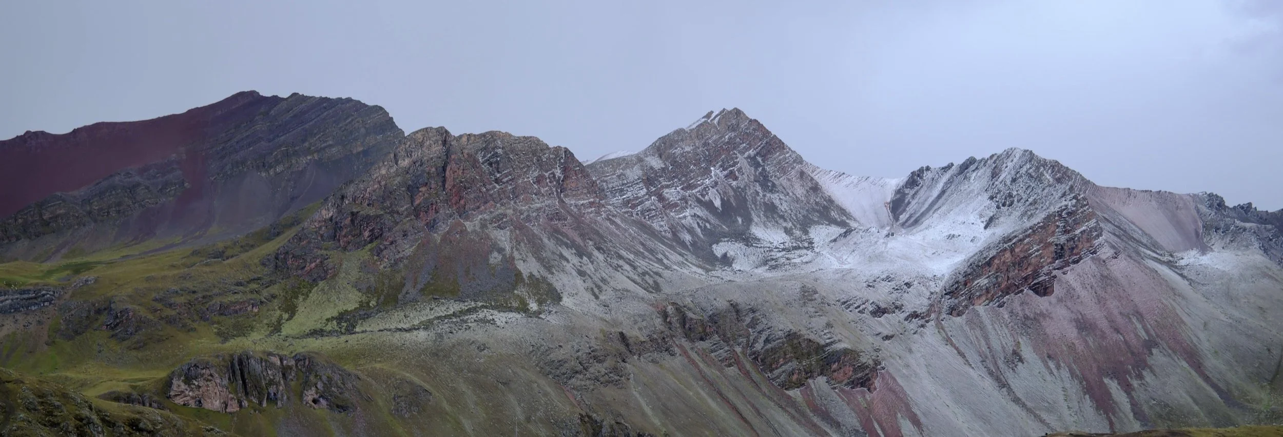 Montañas con nieve en sus picos y vegetación en las laderas, cielo nublado