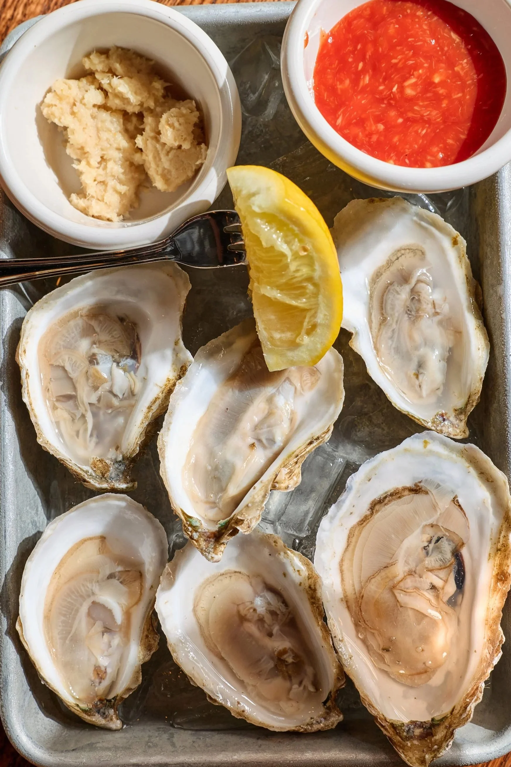 Freshly shucked oysters on a tray with lemon wedge and various sauces in bowls.