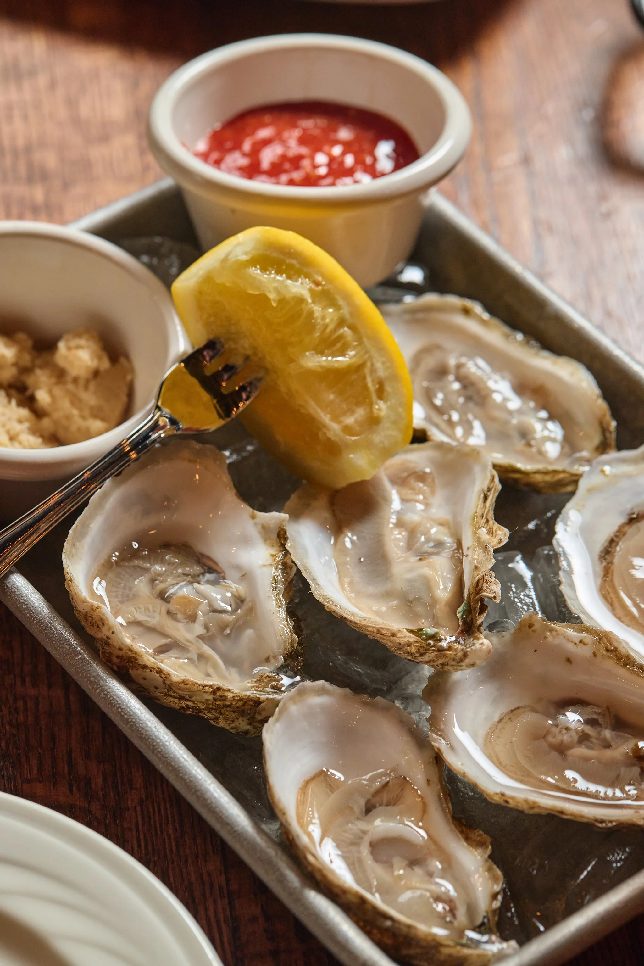 Oysters on a tray served with lemon wedges and dipping sauces.