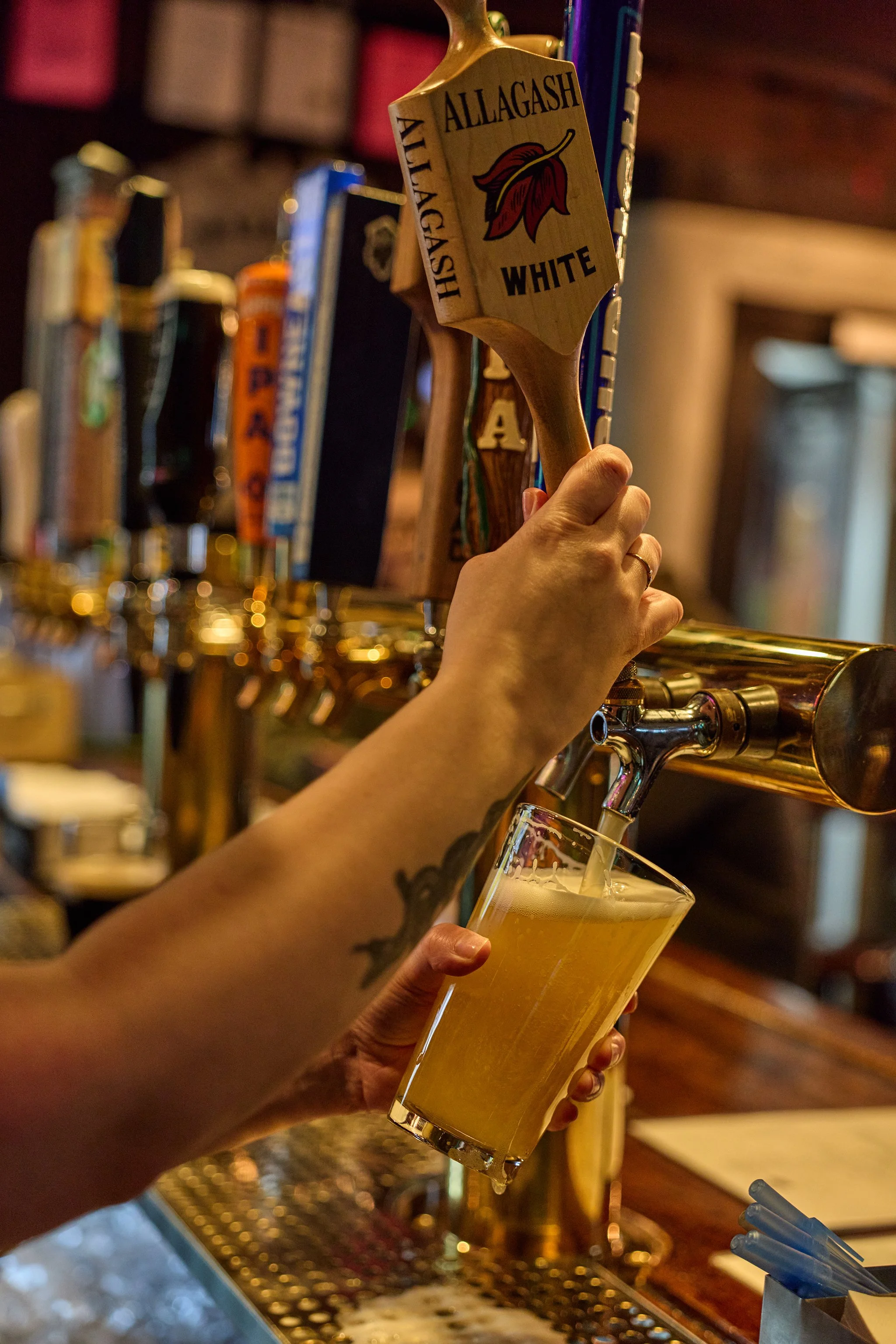A person with tattoos is pouring a glass of beer from a tap at a bar.