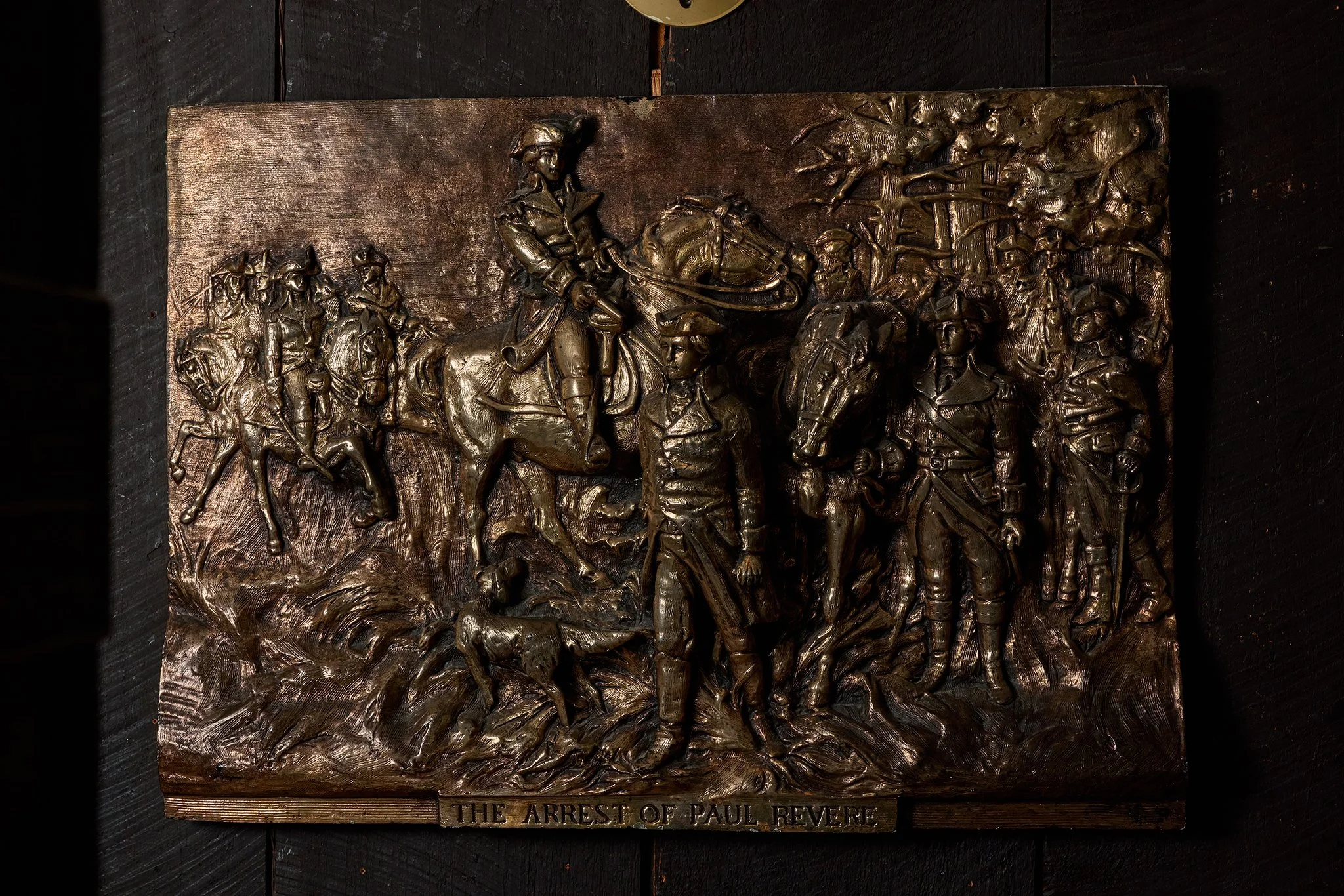 A bronze relief sculpture depicting soldiers and a man on horseback. There is a plaque at the bottom reading 'The Arrest of Paul Revere.'