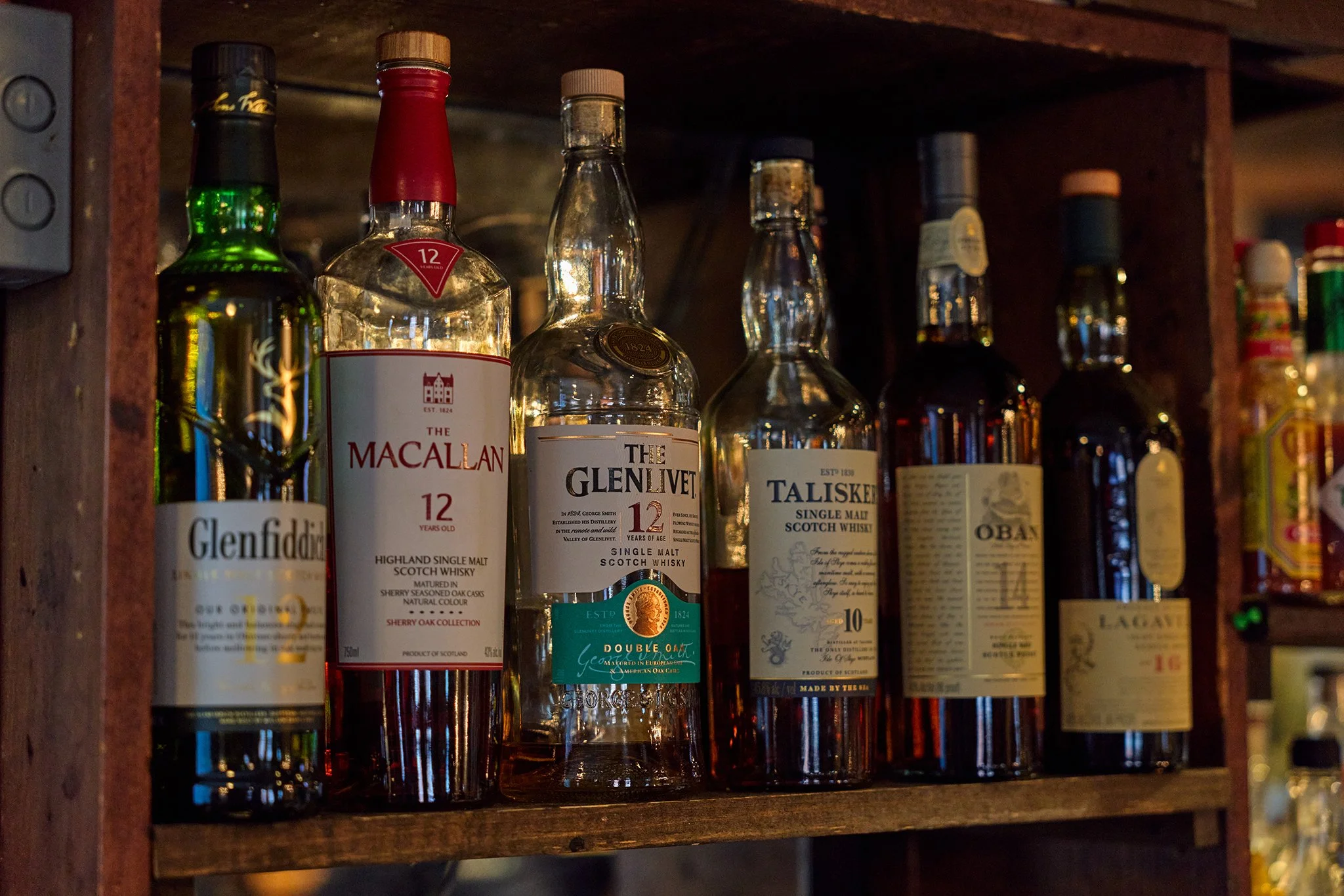 Shelf with several bottles of Scotch whisky, including Glenfiddich, Macallan, The Glenlivet, and Talisker.