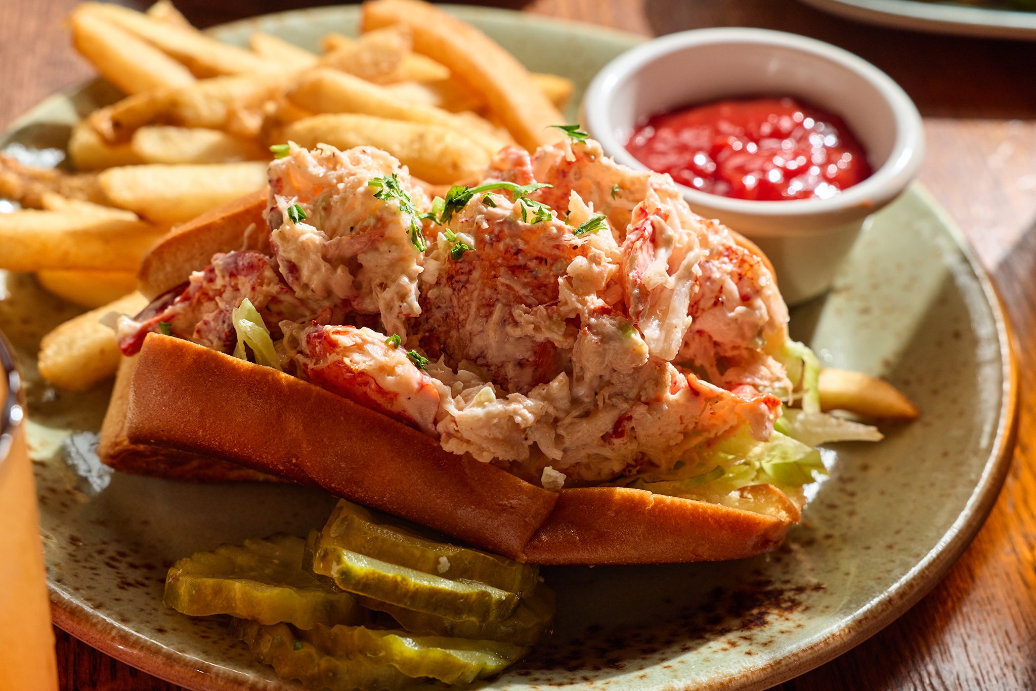 A plate with a sandwich filled with lobster salad, accompanied by French fries, pickles, and a side of ketchup.