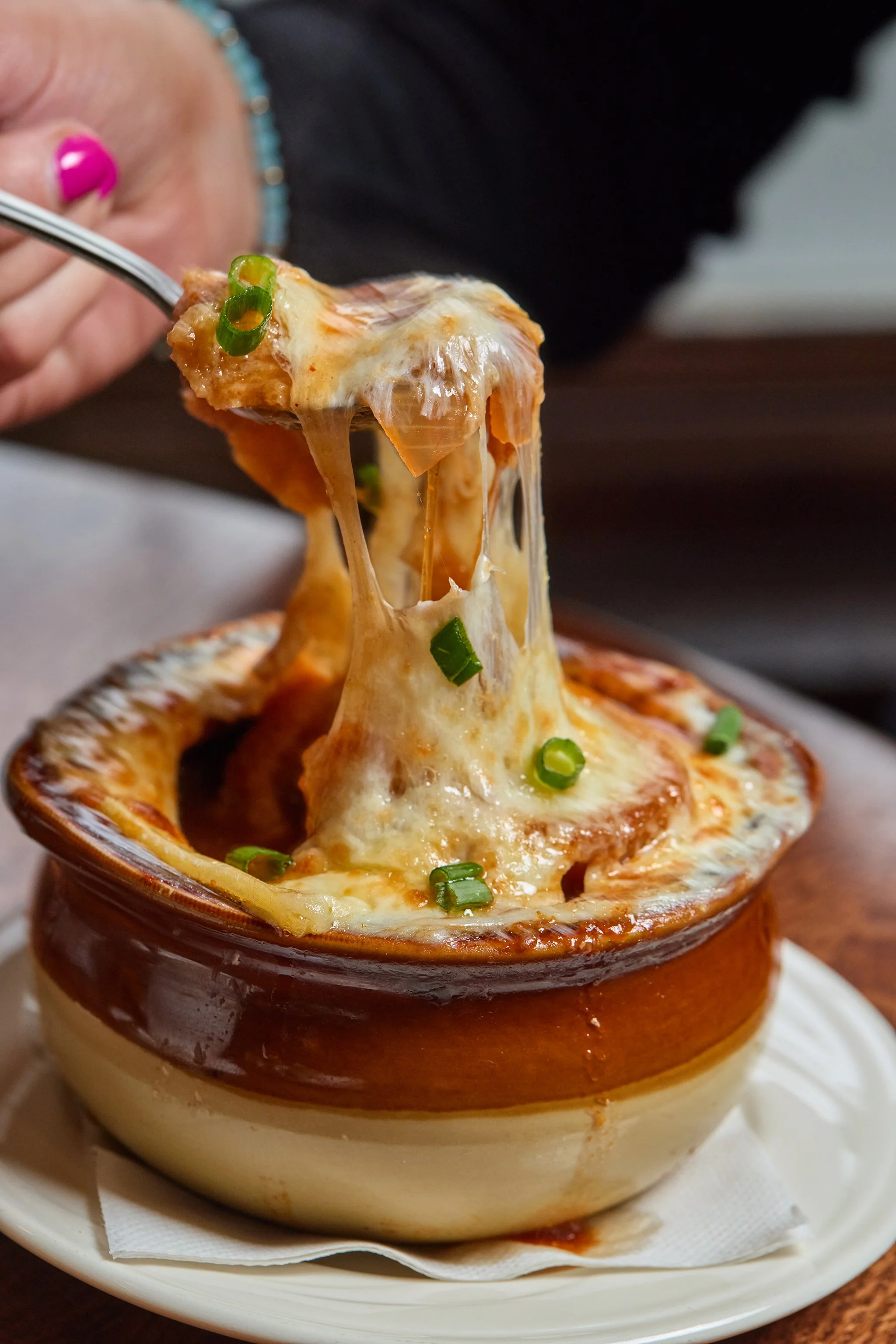 A small brown ceramic bowl filled with baked dish topped with melted cheese and chopped green onions, with a slice of pepperoni visible.