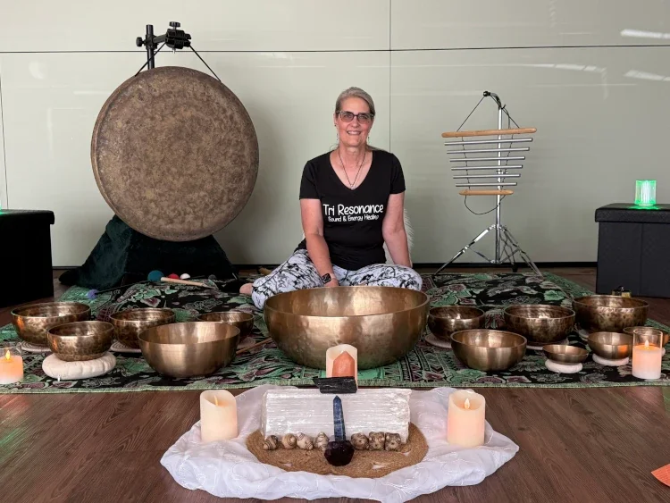 Woman sitting on a patterned rug surrounded by musical and meditation instruments, with candles and decorative objects in front.