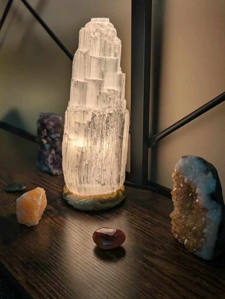 Luminescent salt lamp surrounded by various mineral stones on a wooden table.