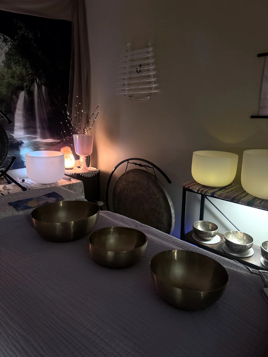 A room with meditation or sound therapy bowls on a table, illuminated soft lighting, a waterfall picture on the wall, and decorative lamps creating a calming atmosphere.