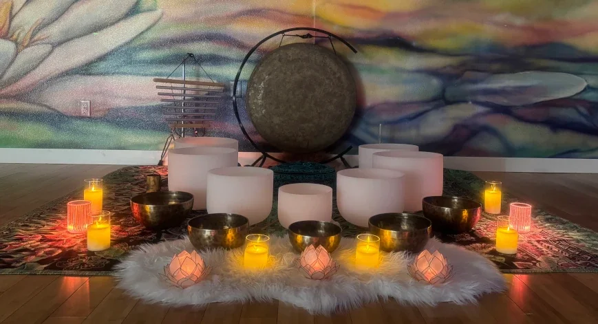 Arrangement of singing bowls, candles, and a gong on a decorative rug with a colorful abstract mural wall in the background.