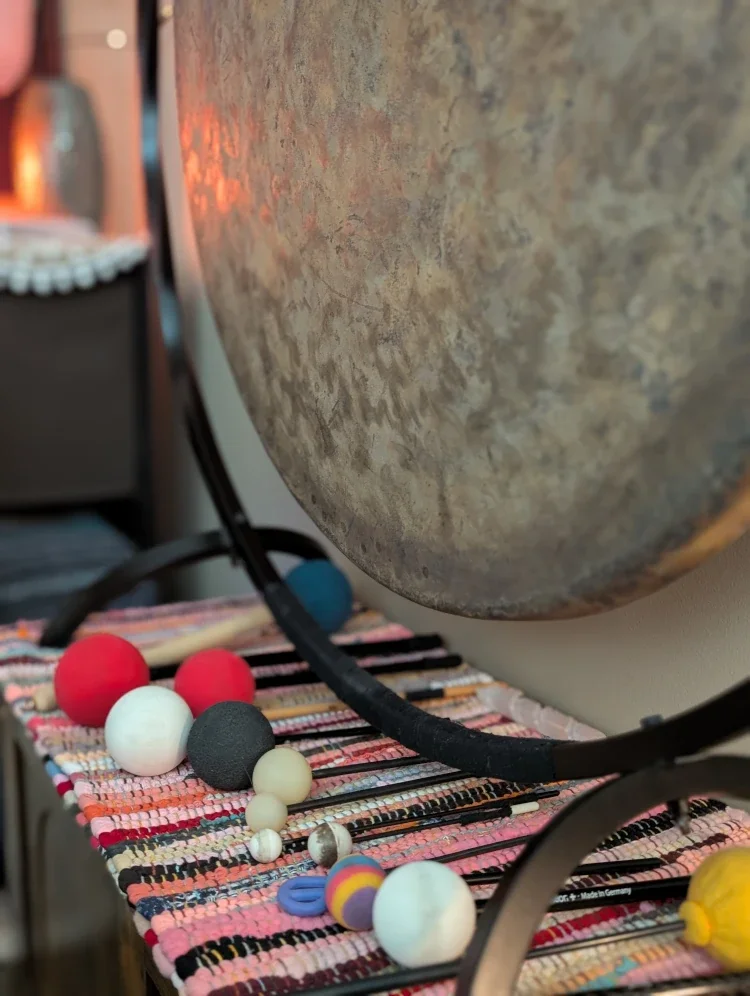 Close-up of a large cymbal on a stand with colorful, textured fabric and small spherical objects on a table below it.