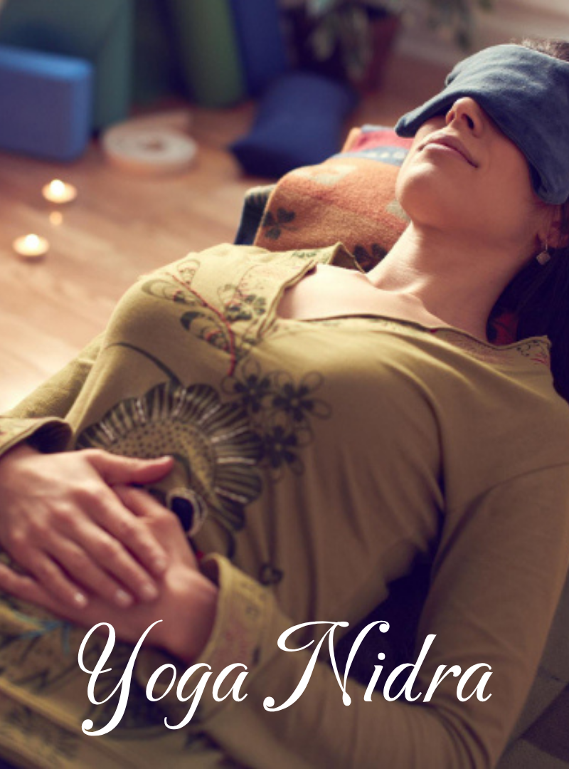 A woman practicing yoga Nidra while lying on her back with a blindfold, hands resting on her abdomen, in a cozy indoor setting with candles and calming decor.