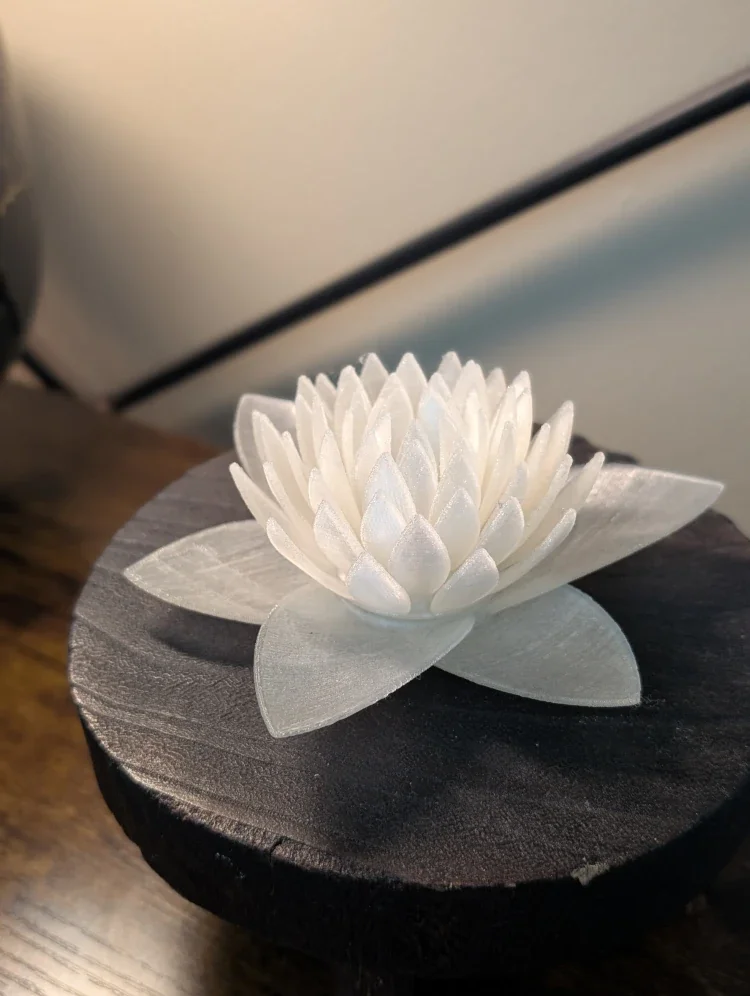 A white artificial lotus flower resting on a black wooden base, placed on a wooden surface.