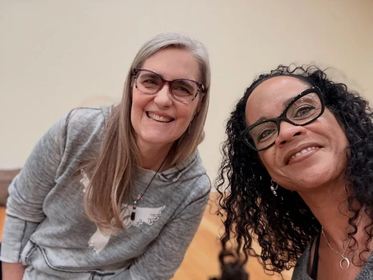 Two women wearing glasses smiling and posing for a selfie in an indoor setting.