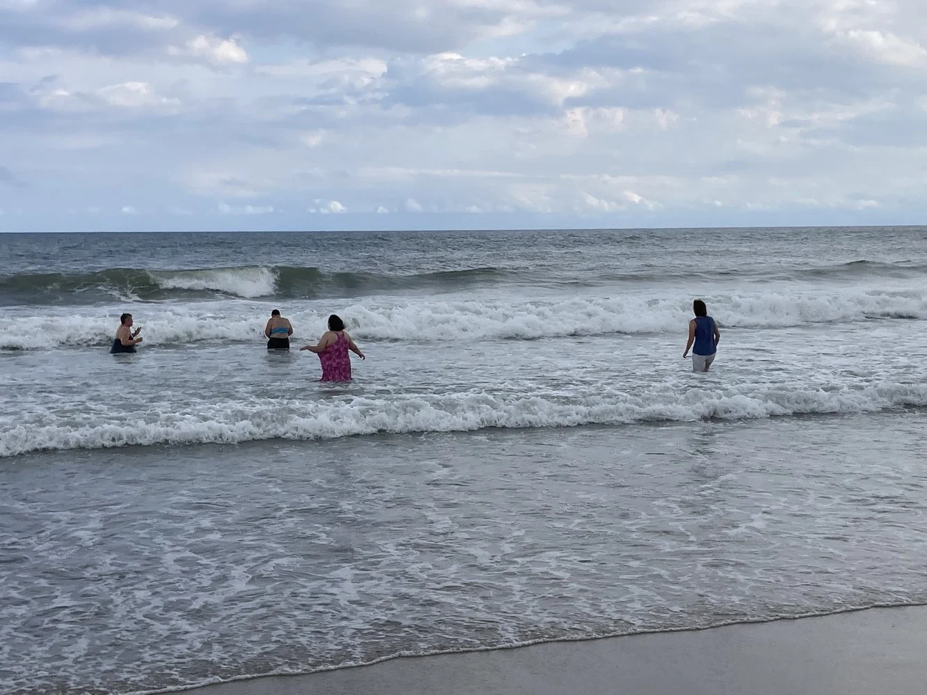 A group of people joyfully wading and playing in the ocean surf on a cloudy day