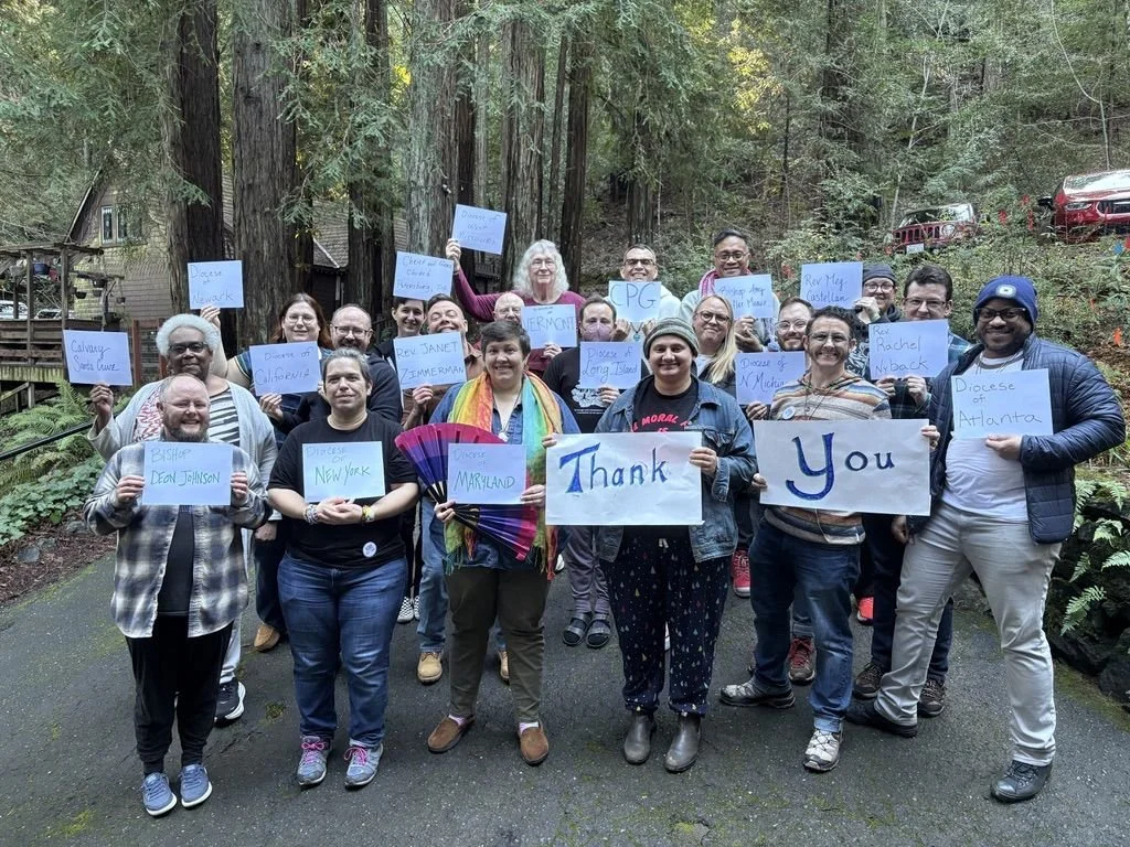 A large group of retreat participants holding handwritten signs saying "Thank You" in a redwood forest