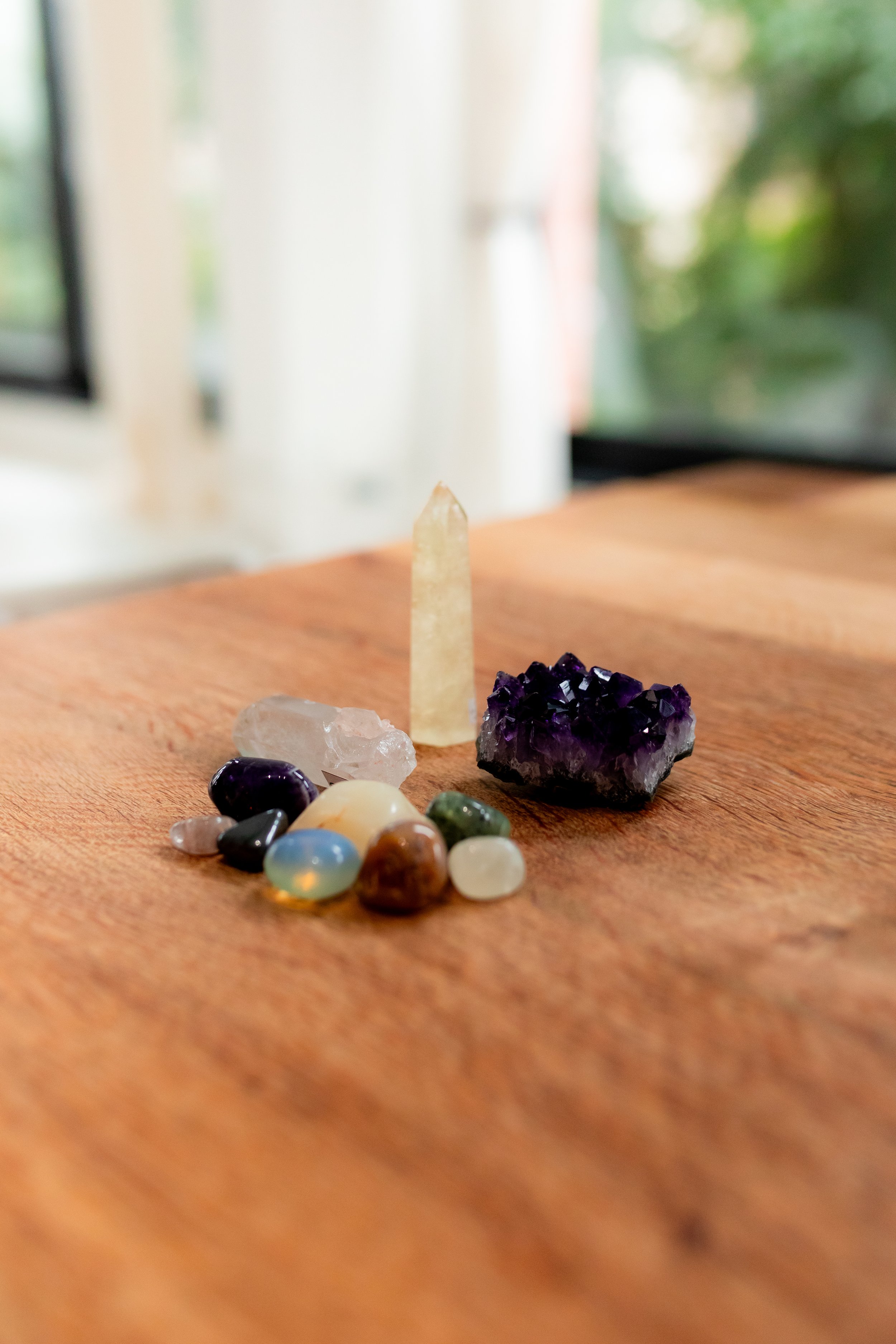 Collection of various polished and raw gemstones and crystals on a wooden surface with a blurred background.