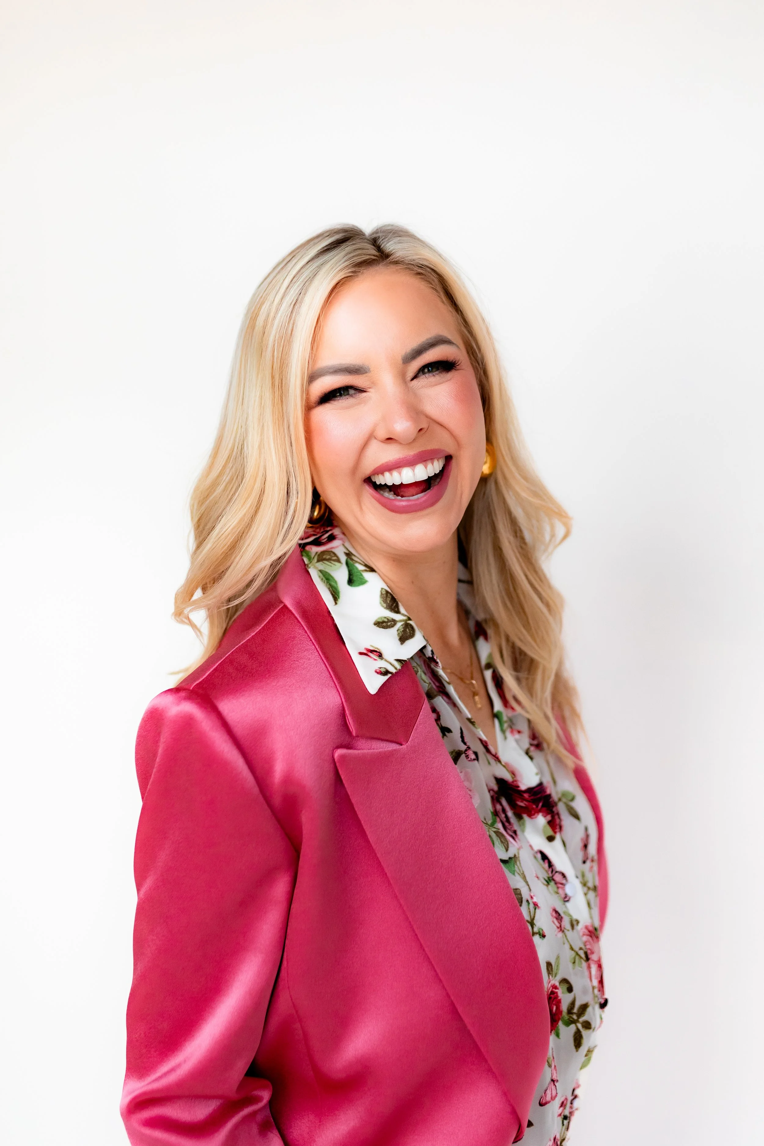 Monica Gostkiewicz smiling and wearing a pink blazer and a floral blouse inside against a white background.