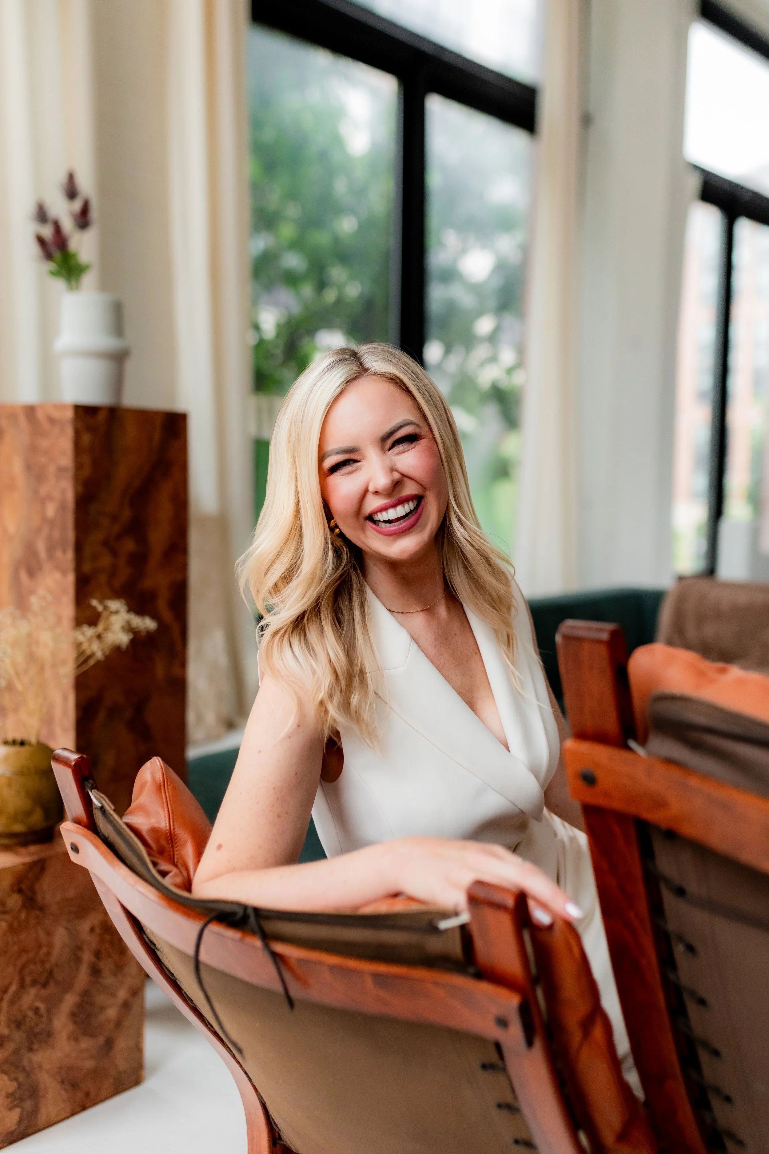 Monica Gostkiewicz wearing a white sleeveless top, sitting in a boat-shaped chair with a smile.