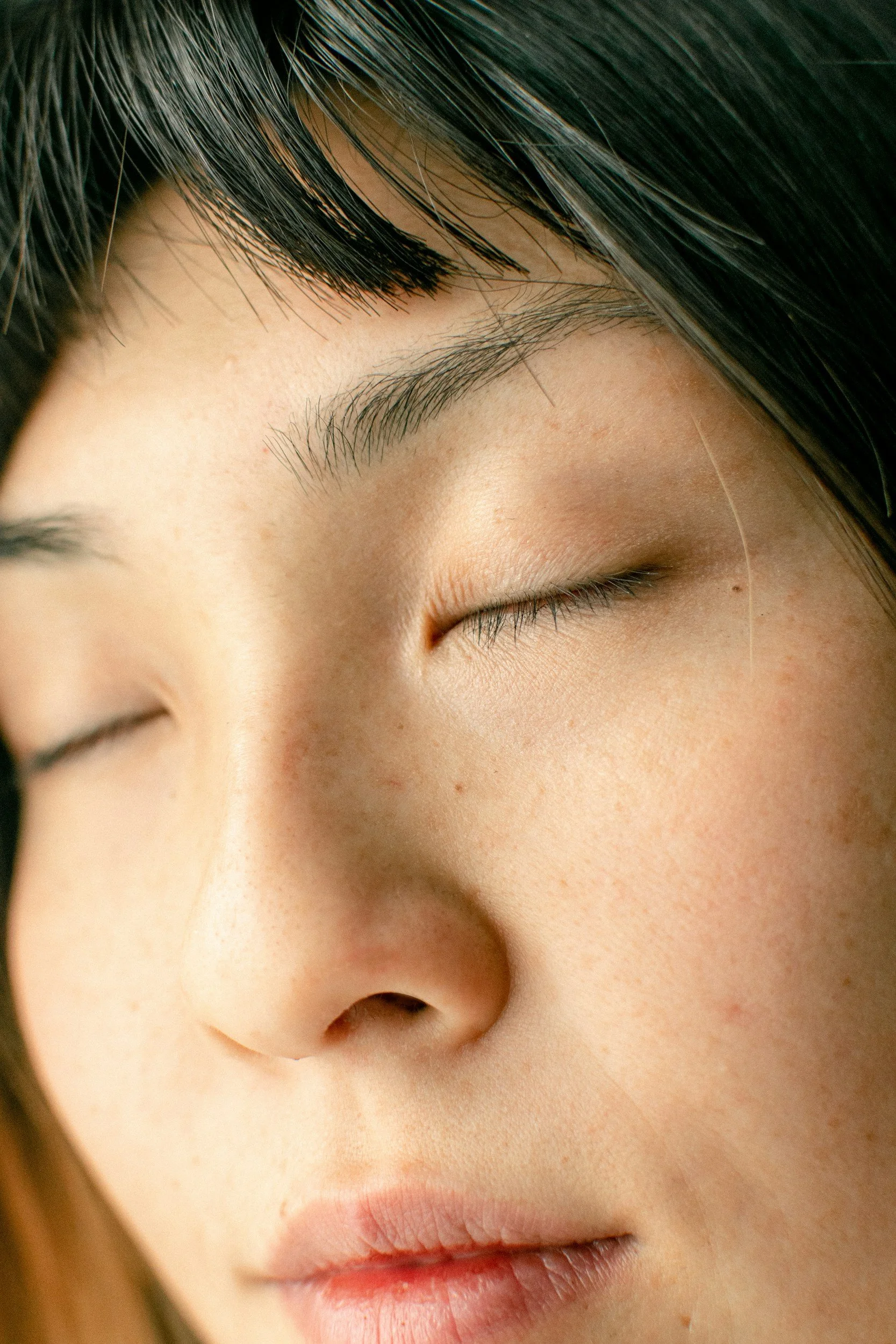 Close-up of a person's face with closed eyes, showcasing their eyebrows, eyelashes, nose, clear skin, and lips.