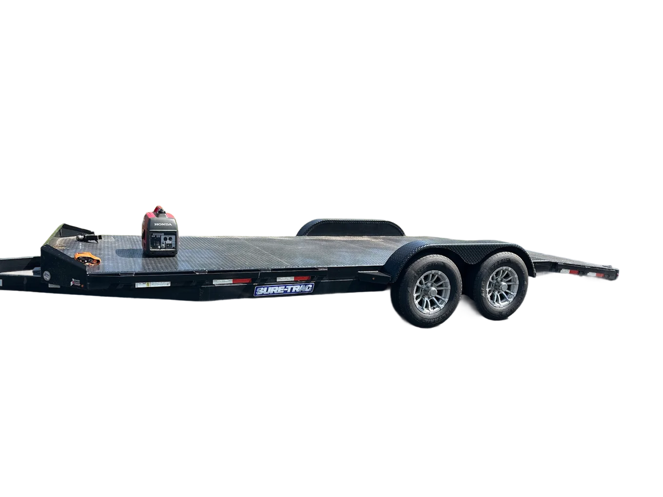 Black flatbed trailer with two axles and new tires, equipped with a small Honda generator, placed on the trailer bed, with a black strap securing the generator.
