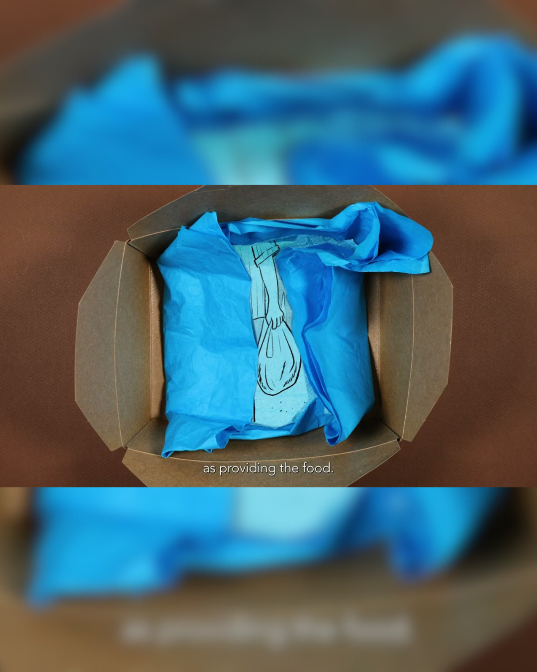 Open cardboard box lined with blue tissue paper containing a drawn illustration of a person carrying a bag of groceries.