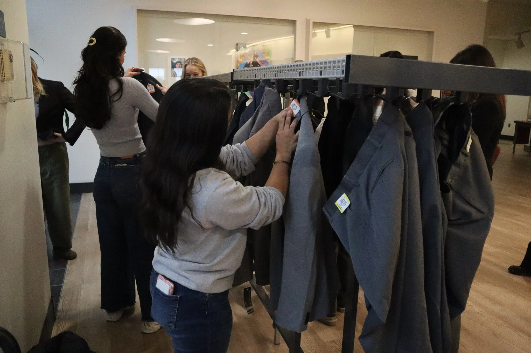 People shopping for clothes at a retail store, looking at hanging shirts and jackets.
