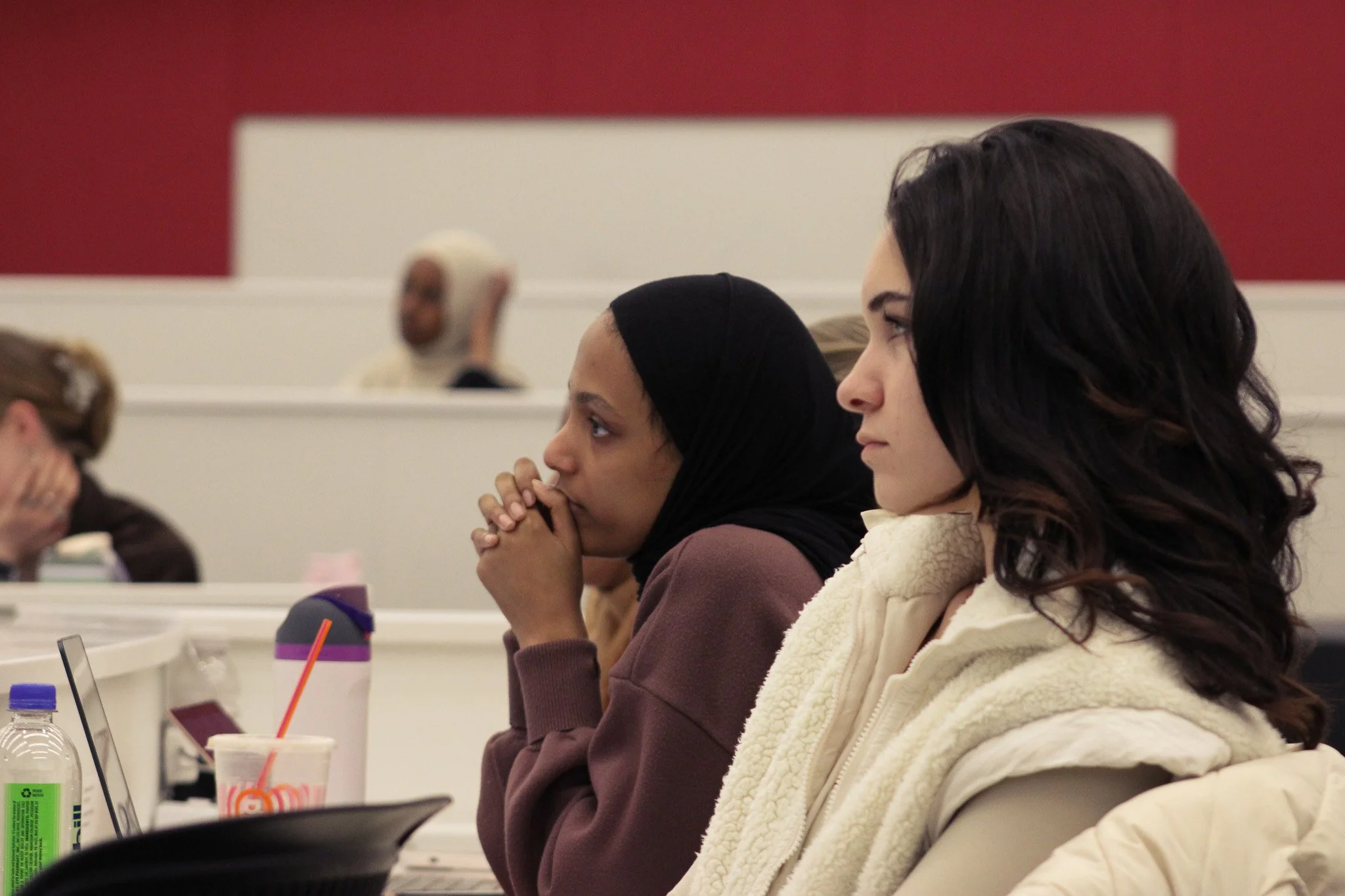 Women sitting at desks in a classroom or conference setting, focused and listening attentively.