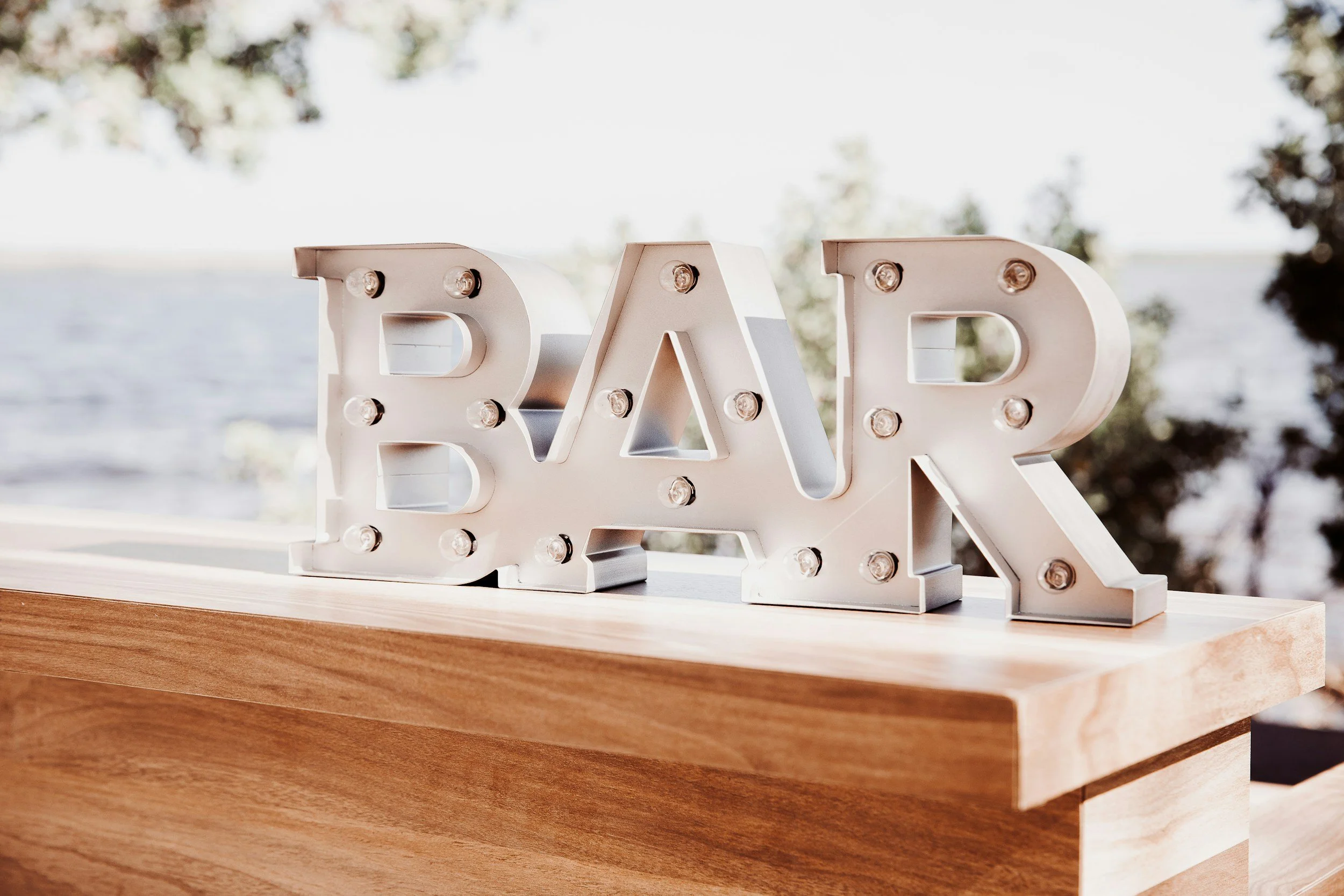 Decorative light-up sign spelling out the word 'BAR' on a wooden surface outdoors.