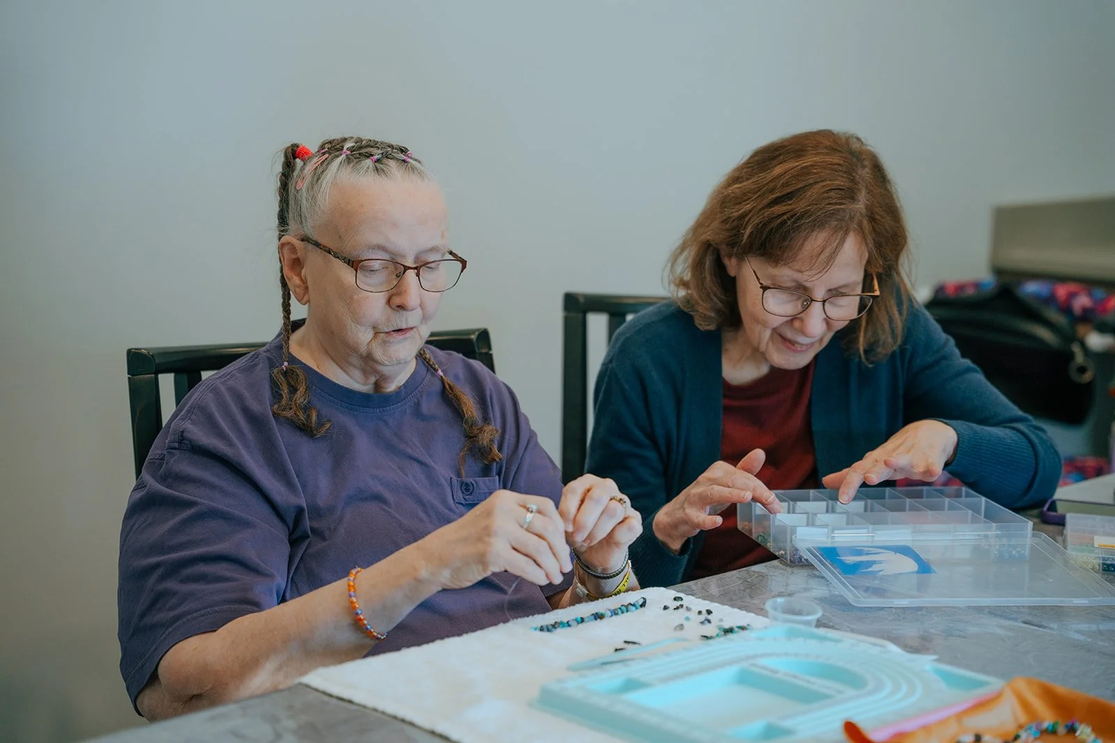 Two older women with glasses enjoy a bead craft activity at a table. Avielle Haven offers engaging long-term residential care, assisted living, and memory care in Midland, MI.