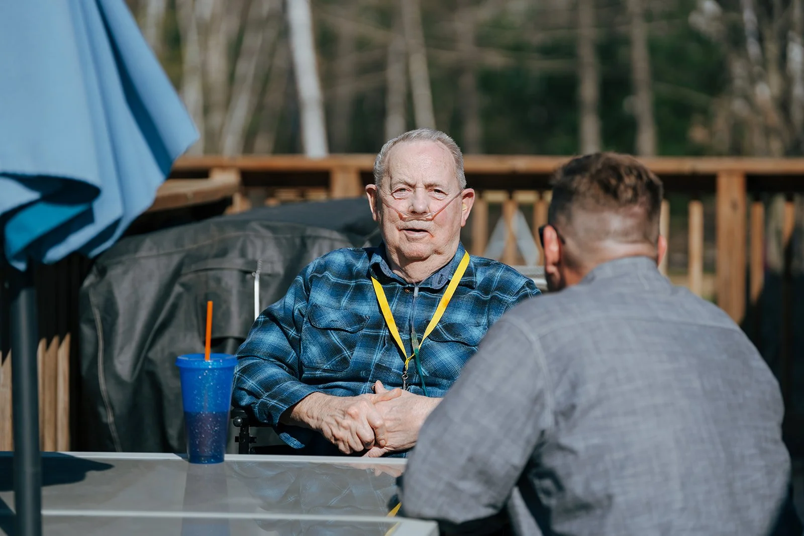 An elderly man with a nasal cannula holds hands with another man outdoors. They relax together during the day at Avielle Haven. We offer compassionate long-term residential care, specialized memory care, and assisted living in Midland, MI.