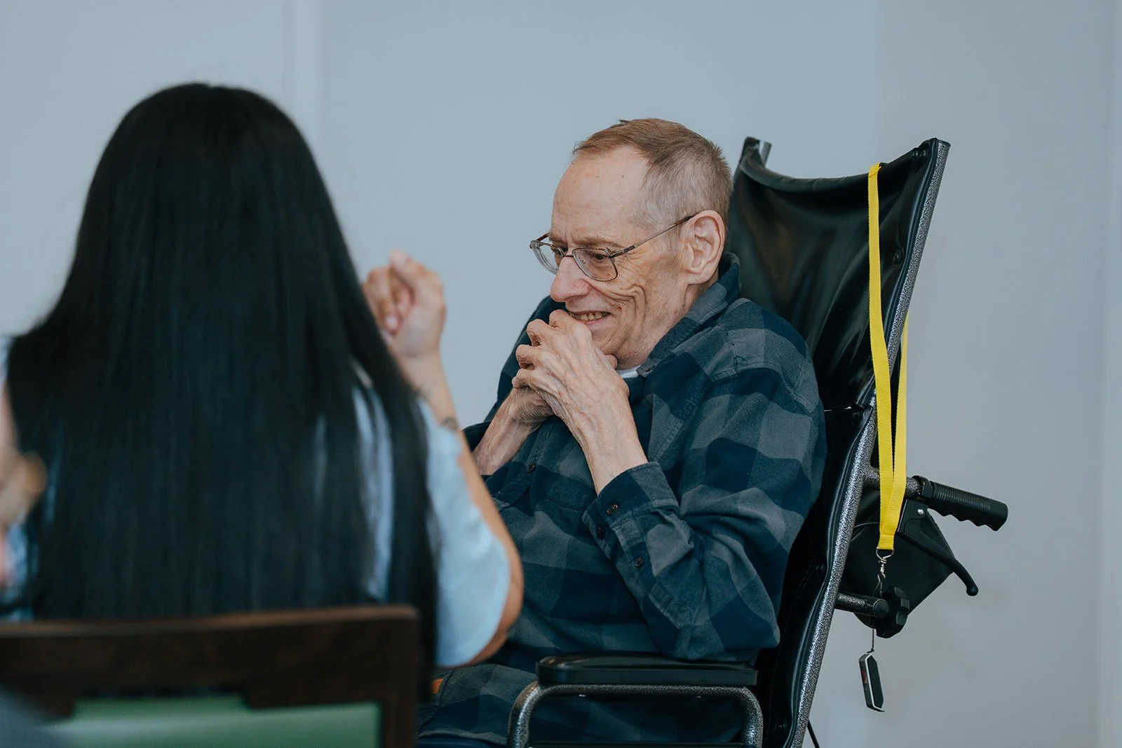 An elderly man in a wheelchair smiles and clasps his hands while talking with a woman. They share a joyful moment. Avielle Haven provides compassionate long-term residential care, specialized memory care, and assisted living in Midland, MI.