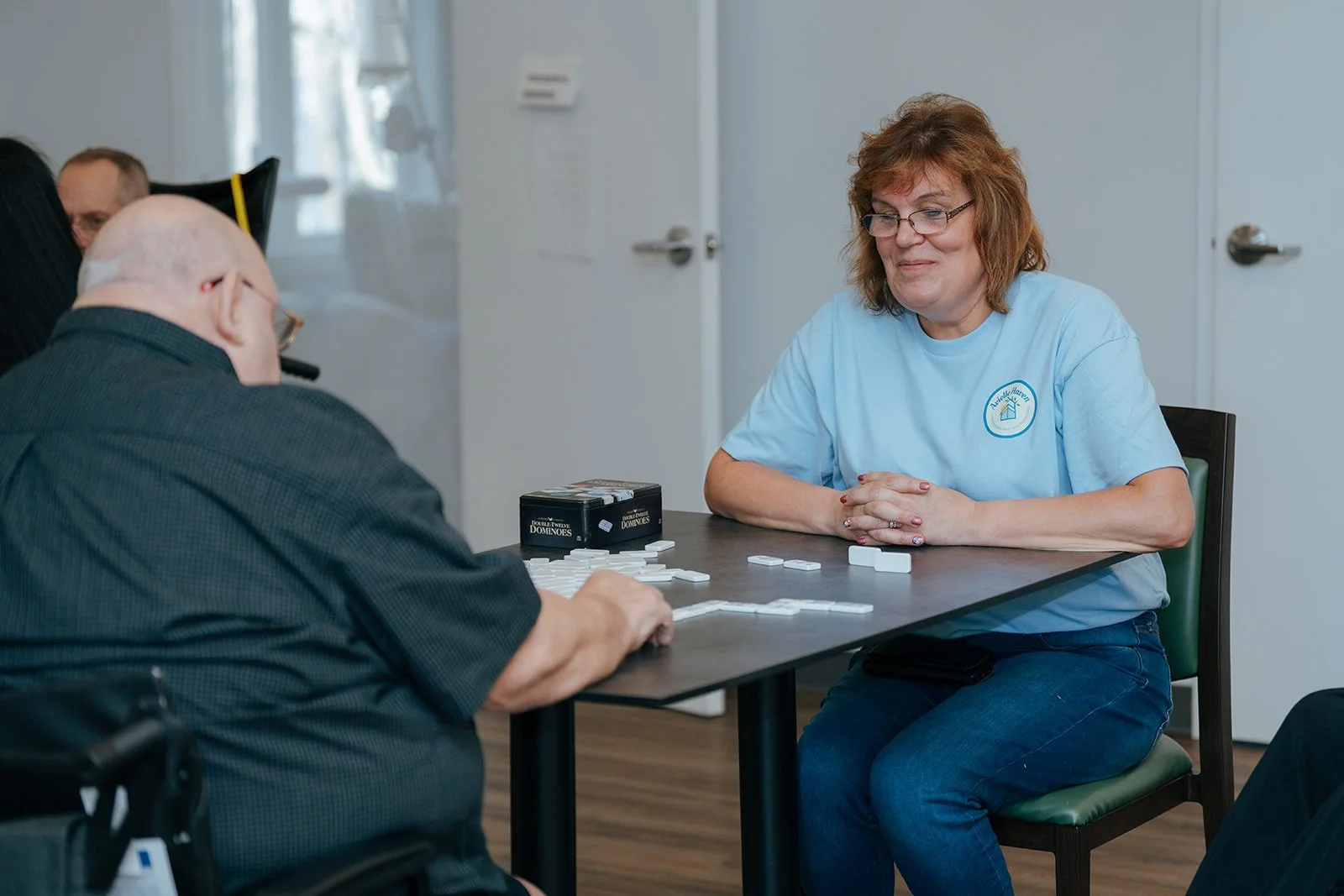 A woman and an elderly man play Dominoes together at a table. Residents enjoy engaging daily activities at Avielle Haven, offering long-term residential care, specialized memory care, and assisted living in Midland, MI.